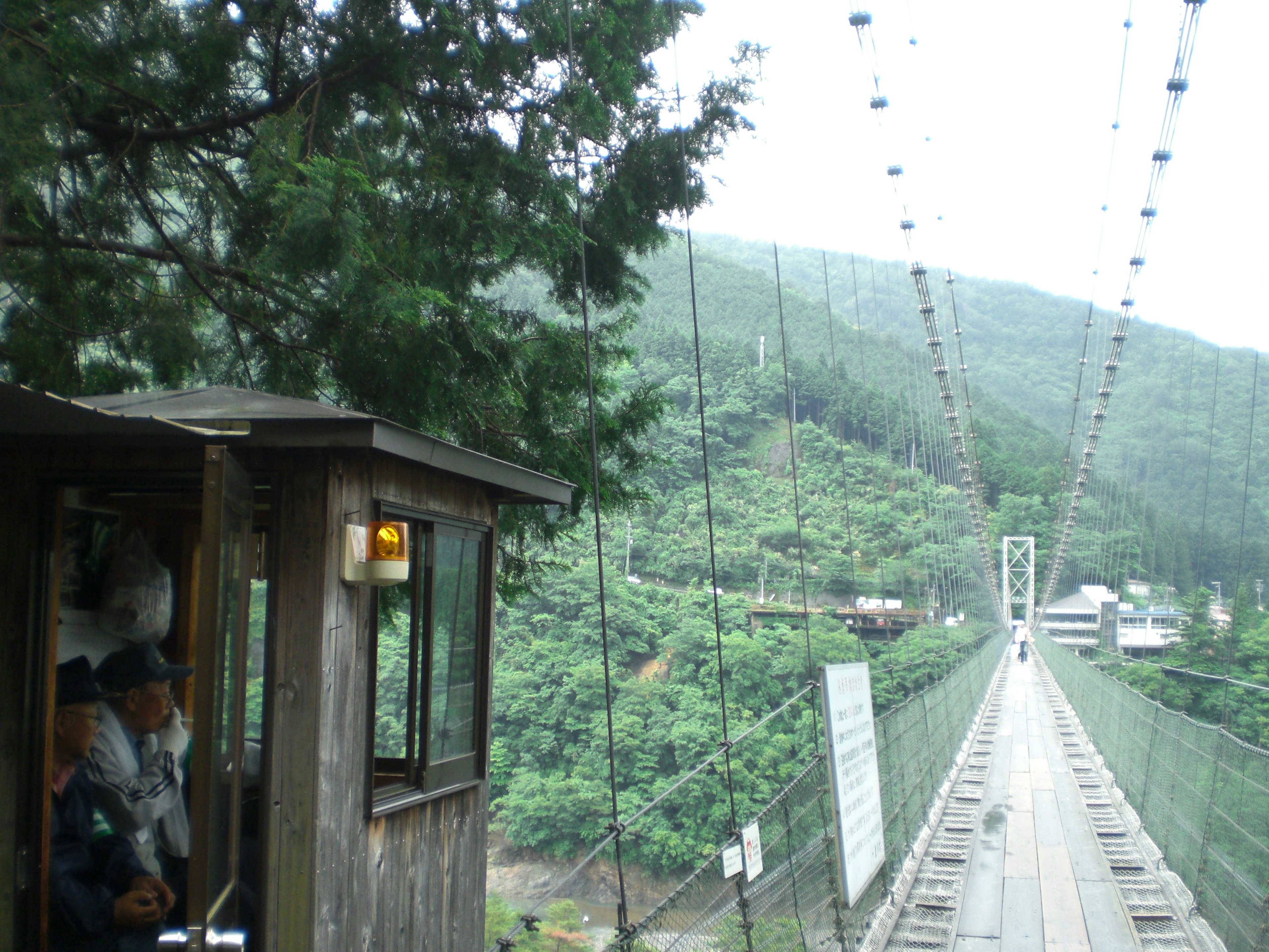 Vista panoramica di un ponte sospeso con montagne verdeggianti sullo sfondo e una piccola cabina