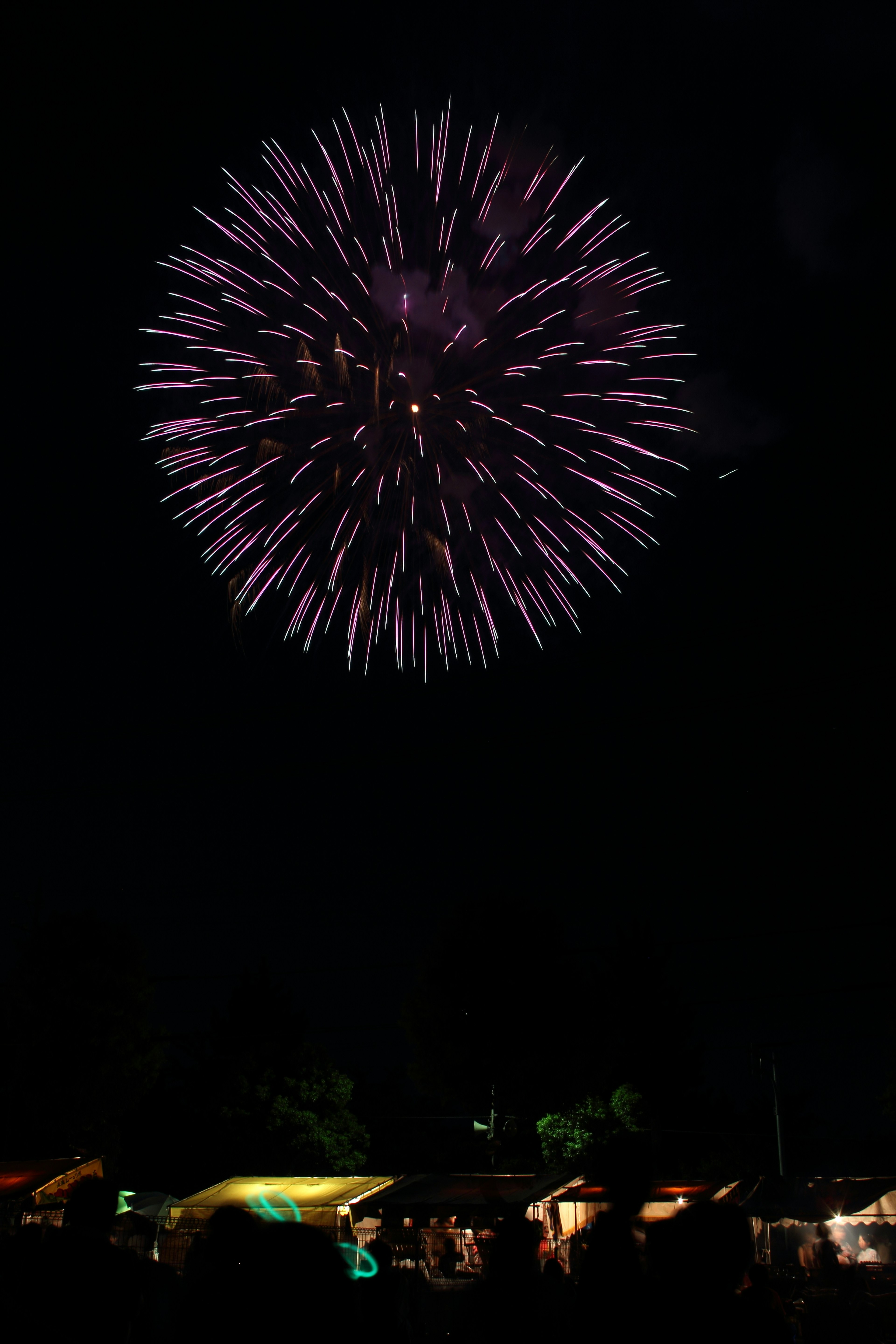 夜空に広がる紫色の花火の爆発とその下にある屋台