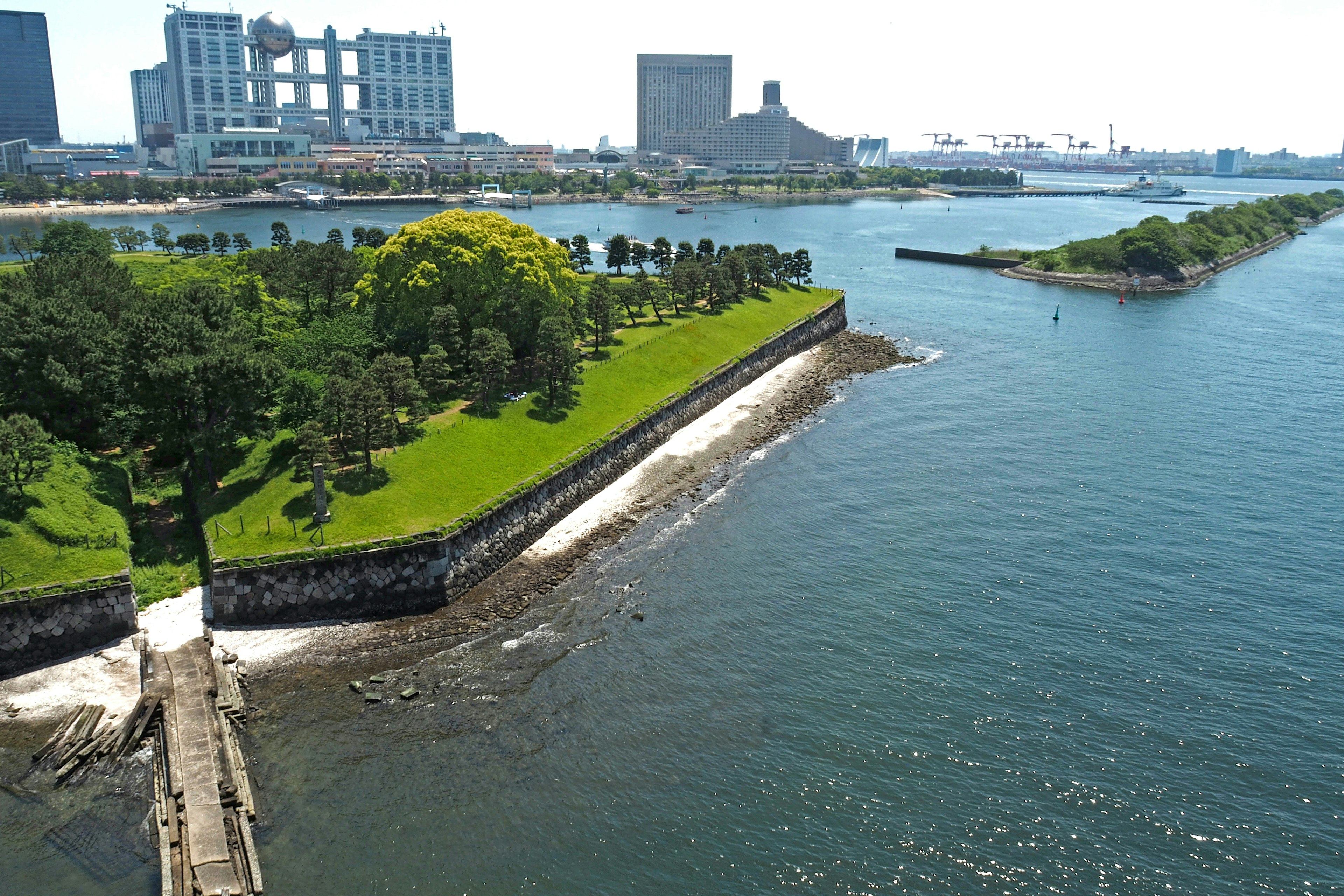 Scenic view of a lush green park along the water with urban buildings in the background