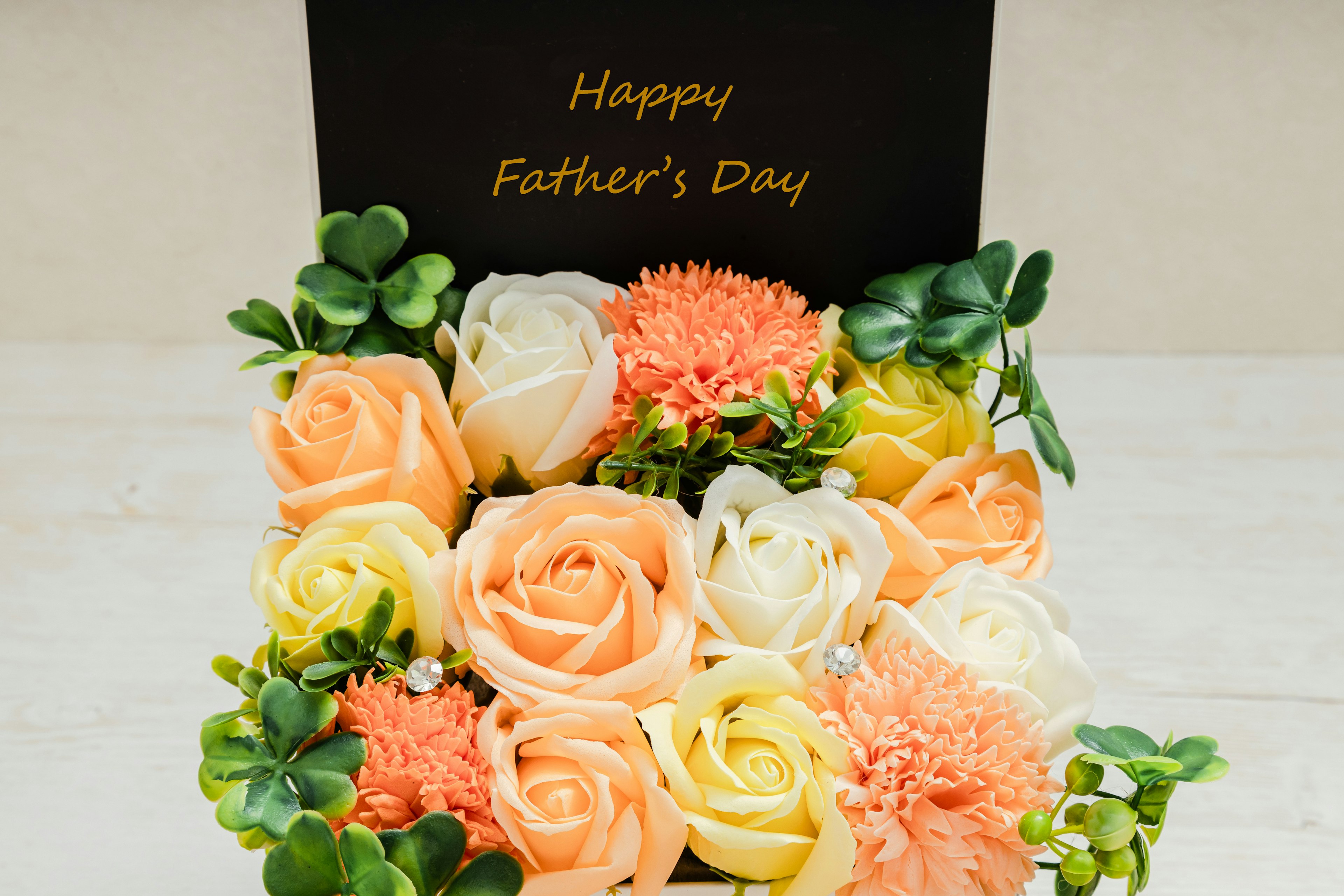 A flower arrangement featuring orange and white roses and carnations in a black box with a Father's Day message