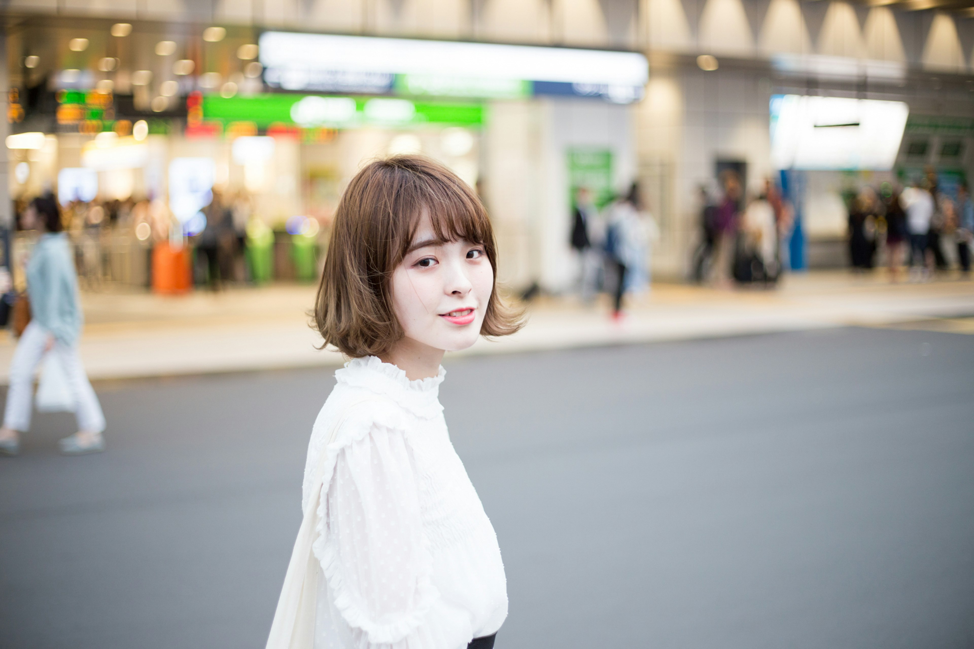 Portrait of a smiling woman in the street wearing a white blouse with a station sign in the background