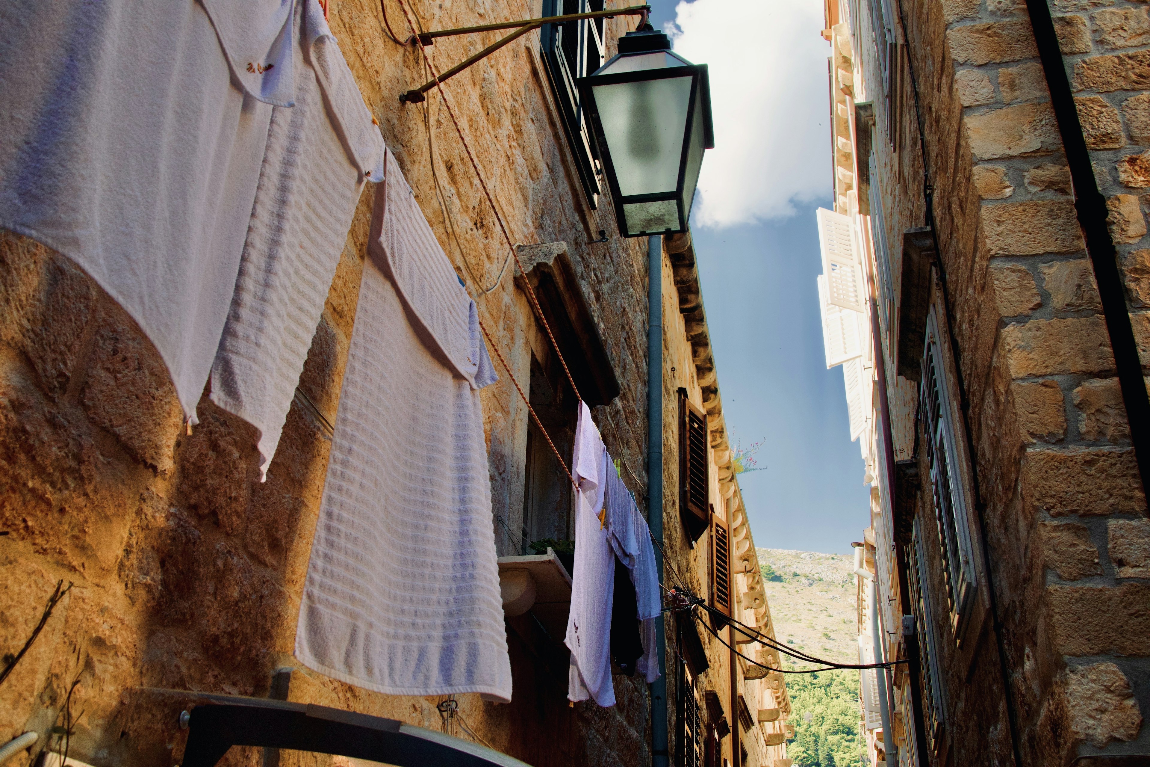 Ruelle étroite en pierre avec du linge blanc suspendu et un lampadaire