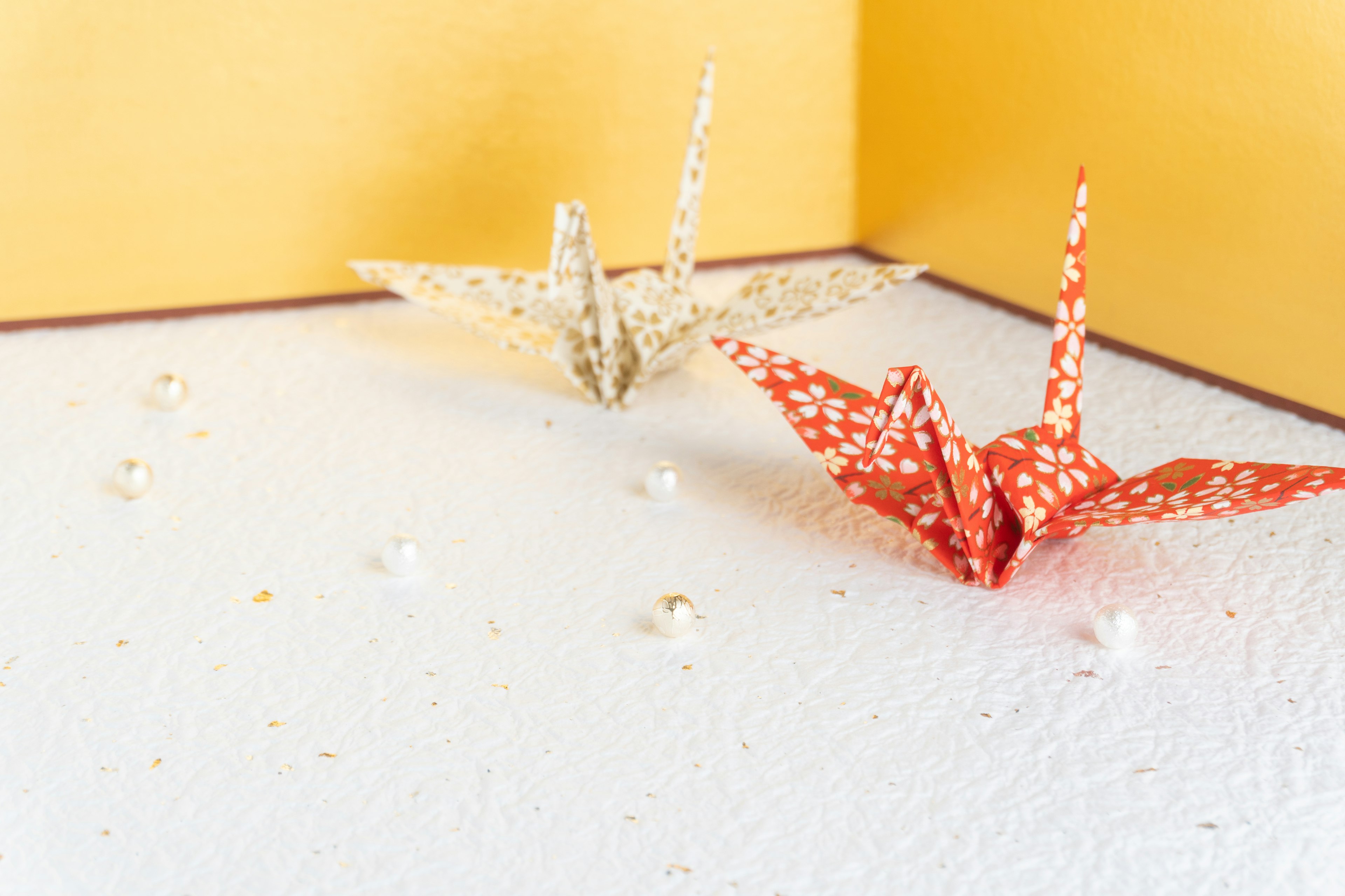 Red and white origami cranes on a white table with a golden background