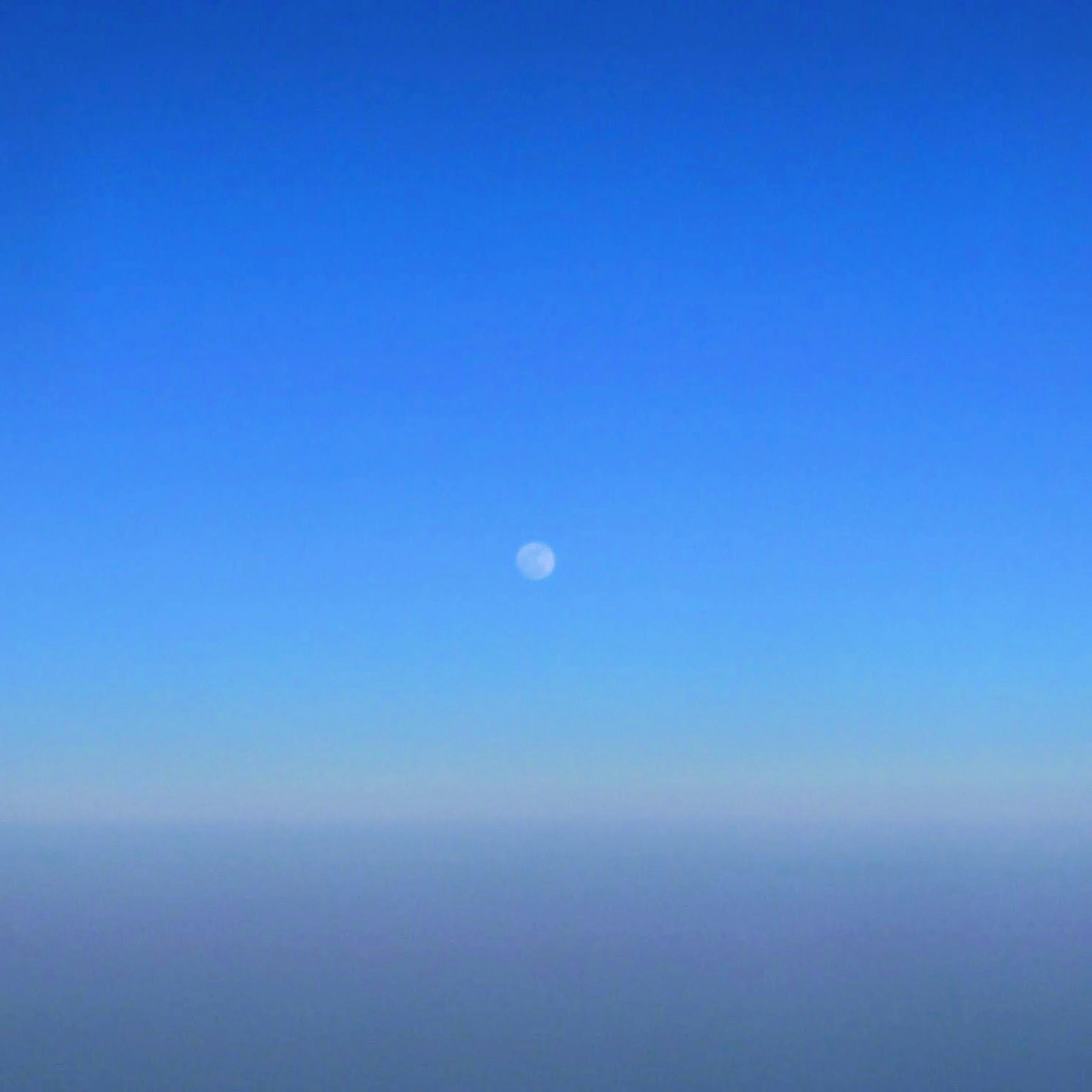 青空の中に小さな月が浮かんでいる風景