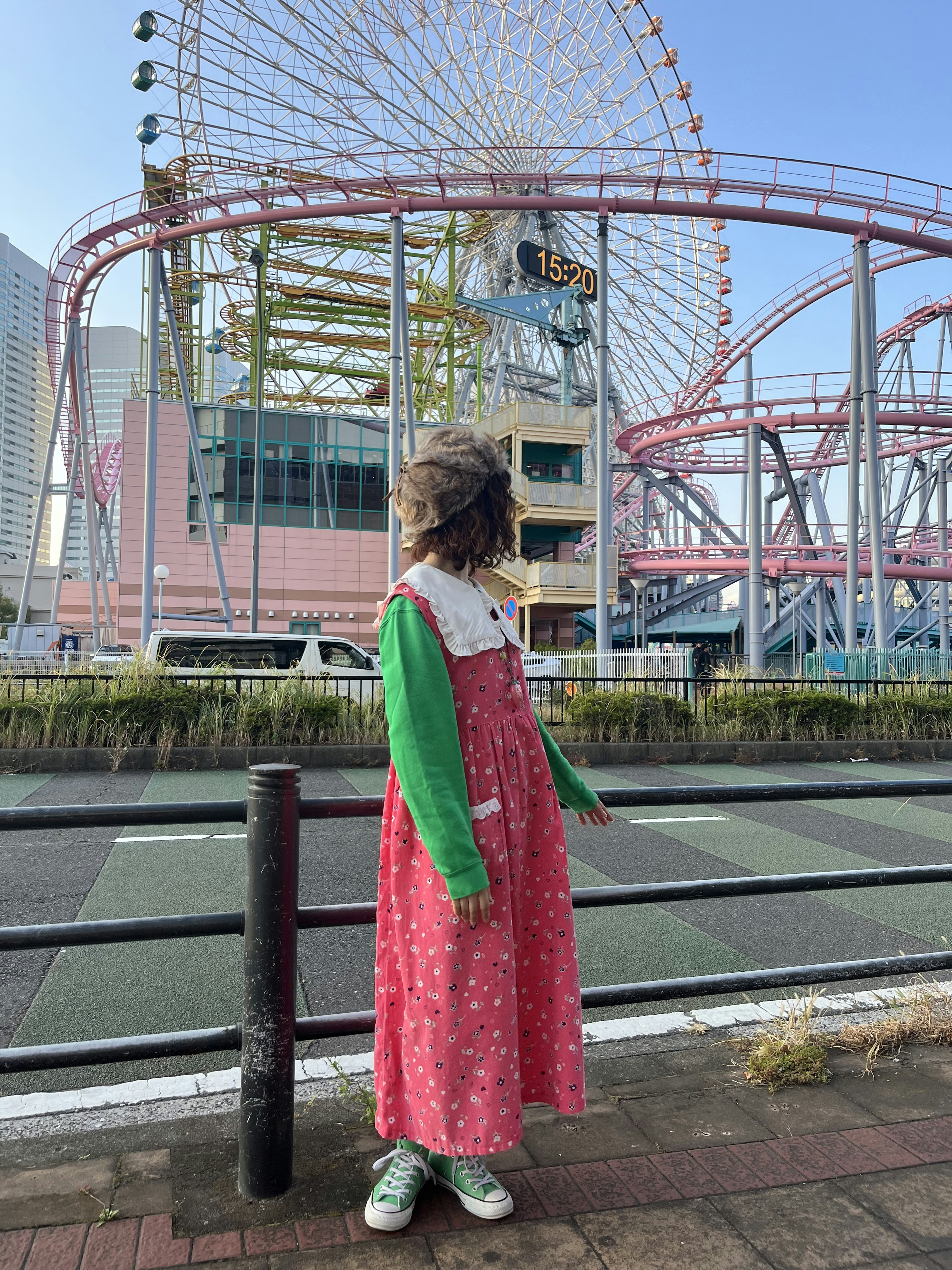 Ragazza in piedi davanti a una ruota panoramica, indossa un vestito con maniche verdi e un vestito rosa