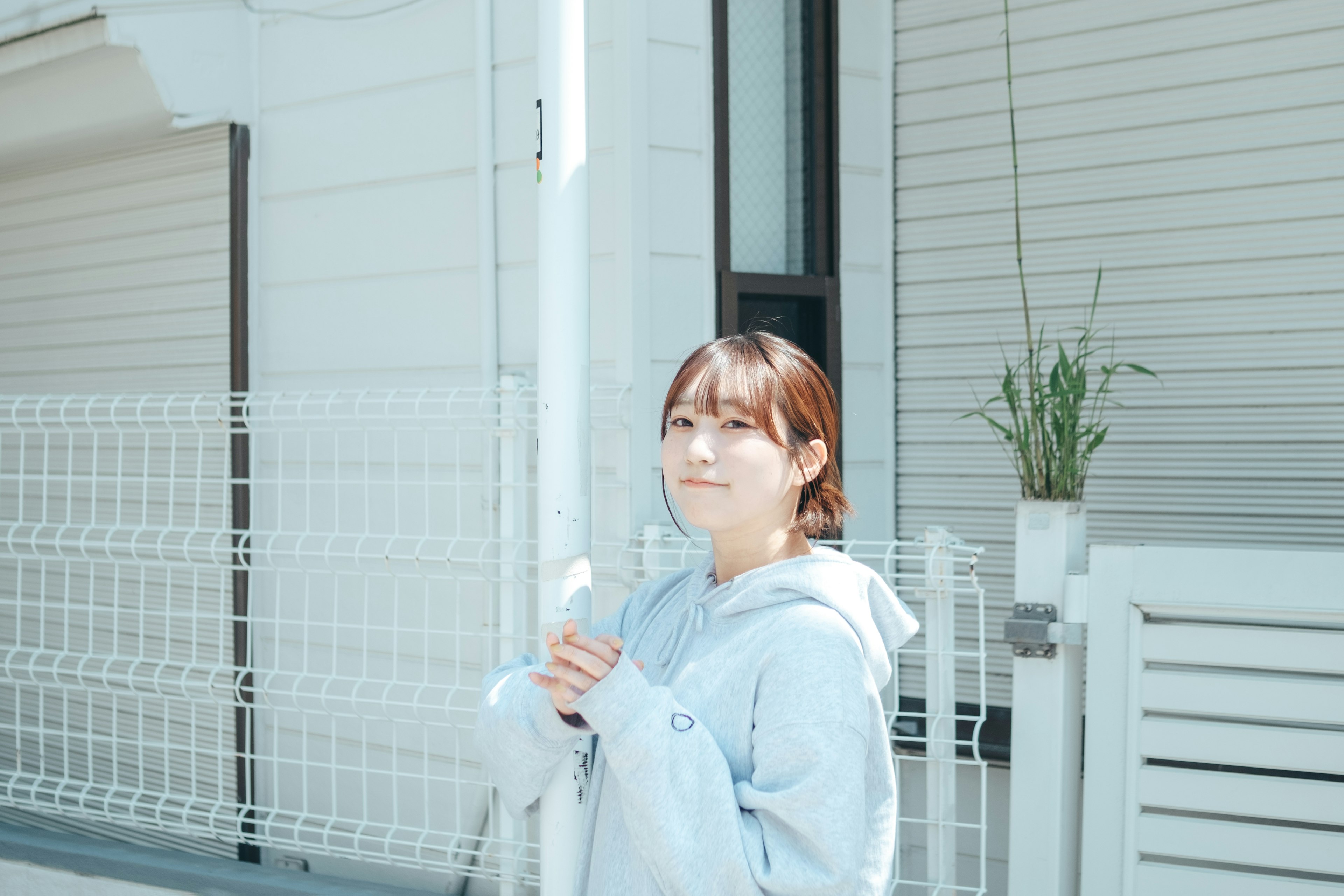 A young woman smiling in bright sunlight standing in front of a white house