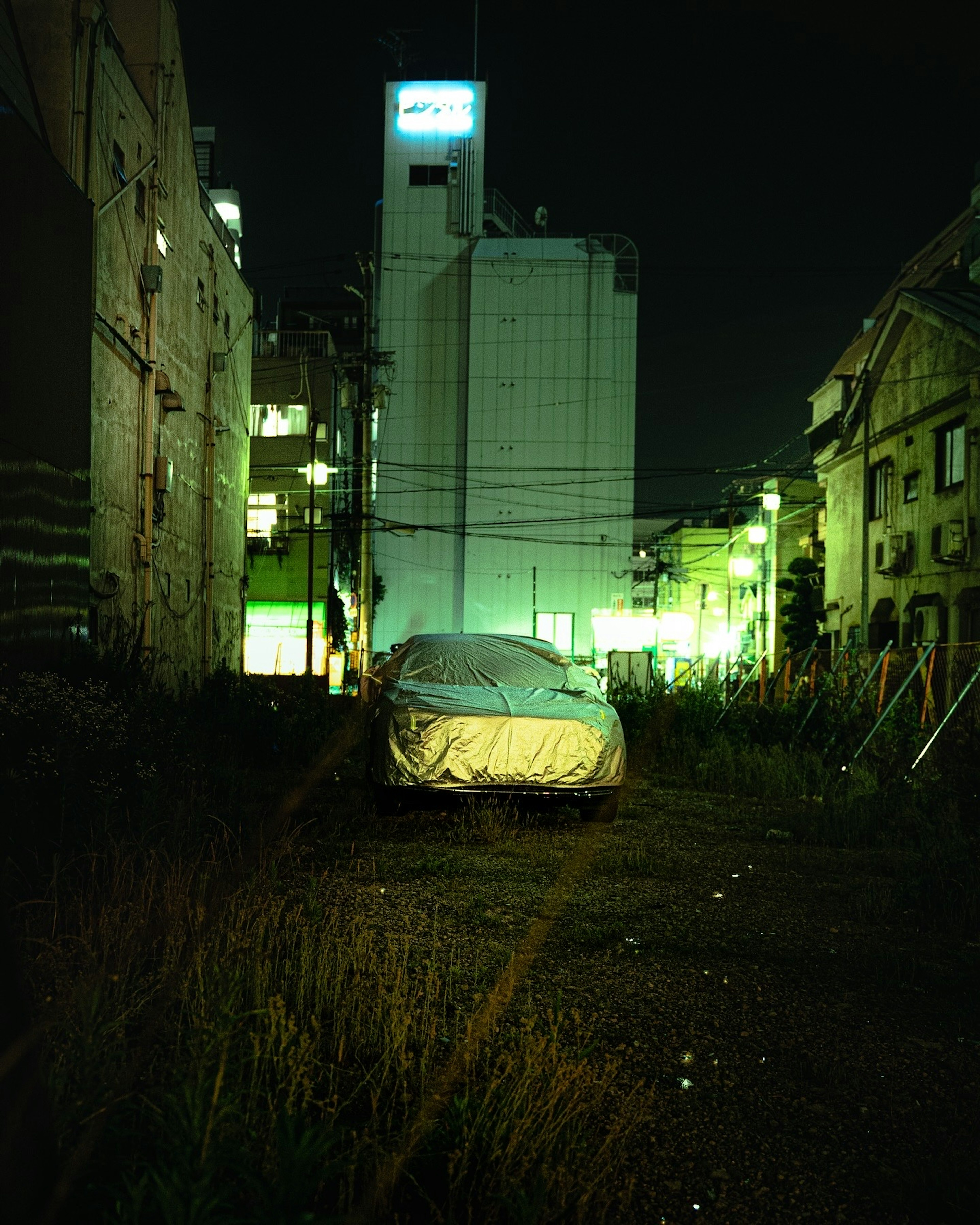 Ein bedecktes Auto in einer urbanen Umgebung, beleuchtet von grünen Lichtern bei Nacht