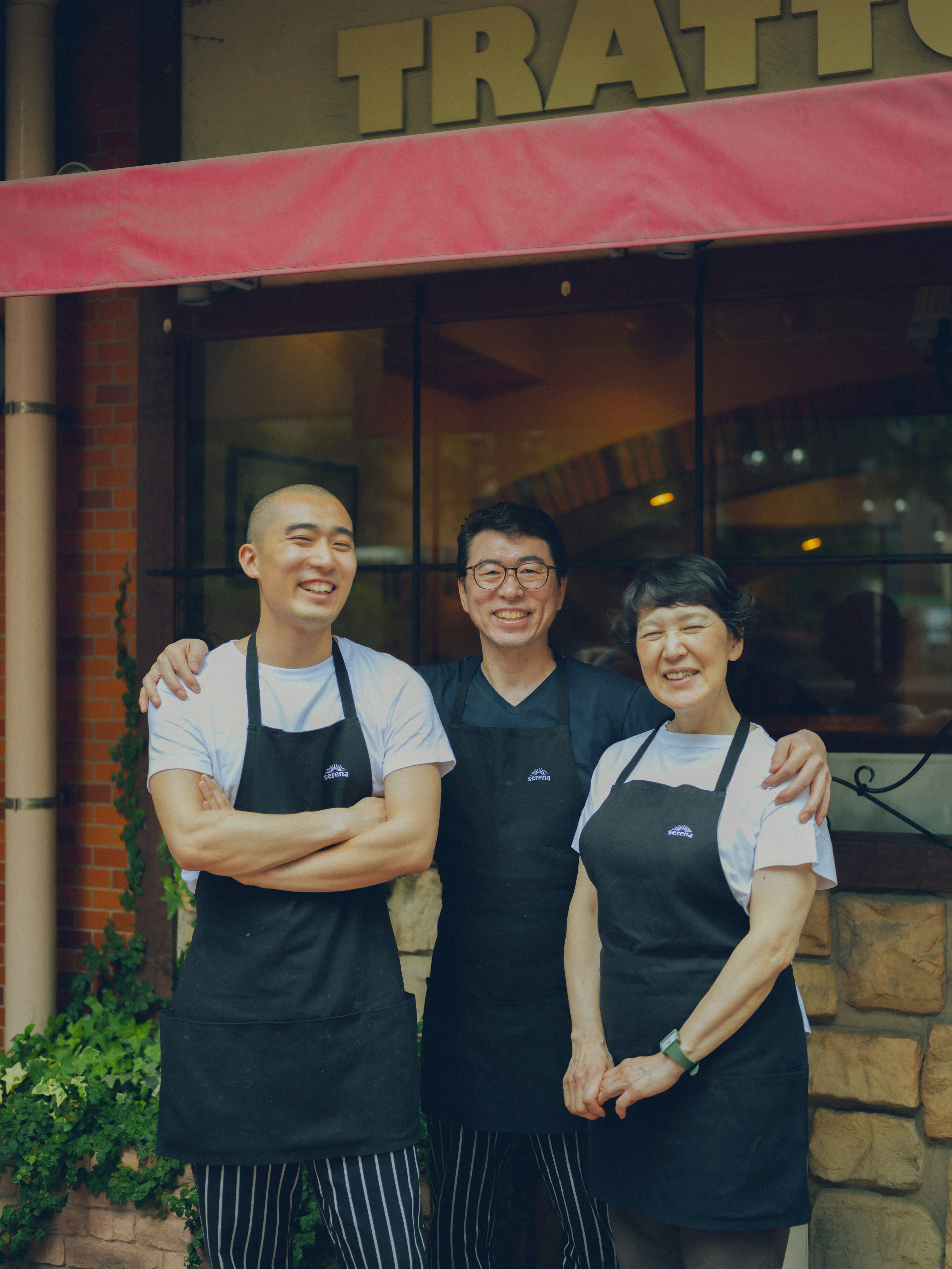 Tre membri dello staff sorridenti in posa davanti a una trattoria