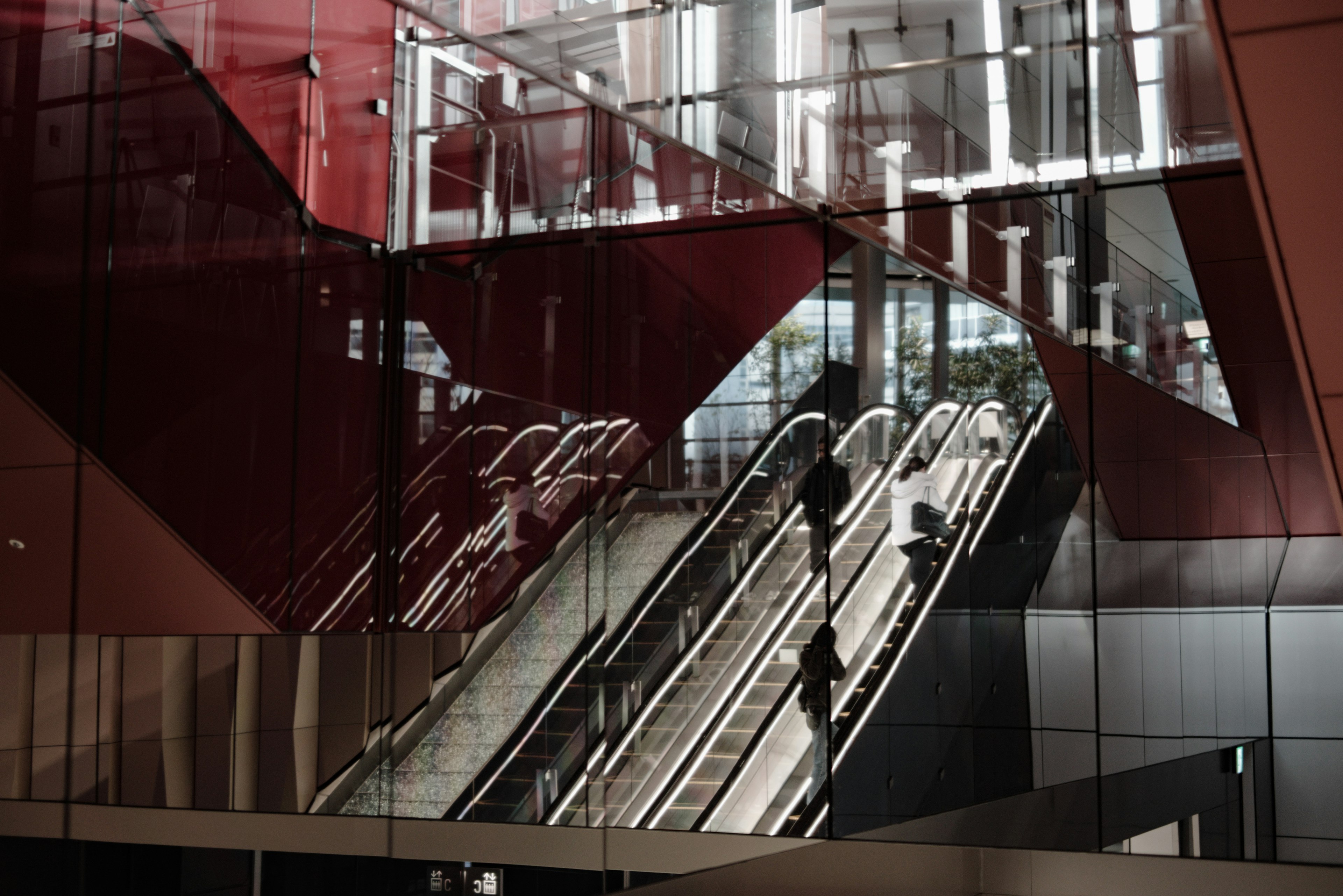 Vue intérieure avec un escalier roulant moderne et des reflets de murs rouges