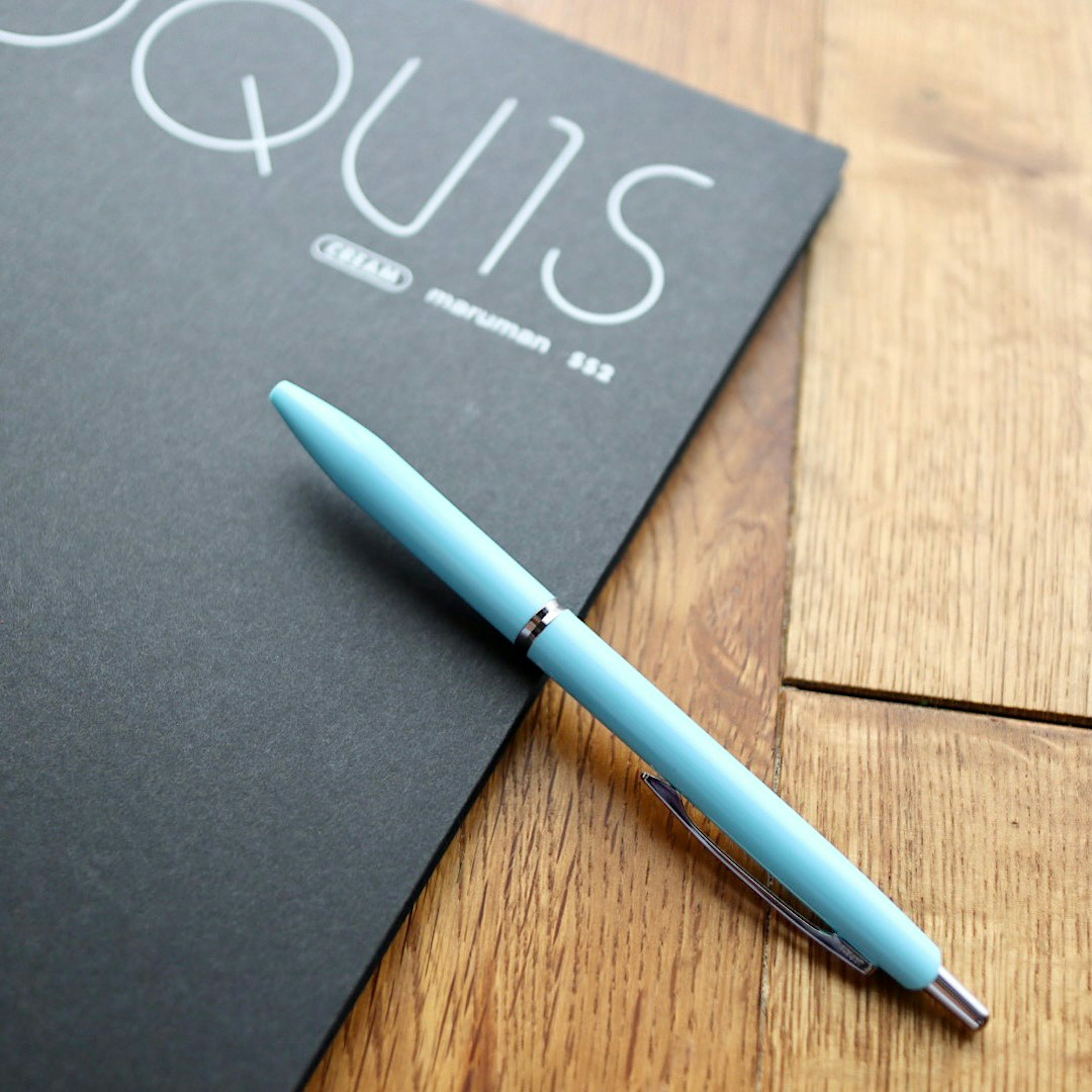 A blue pen resting on a black notebook on a wooden table