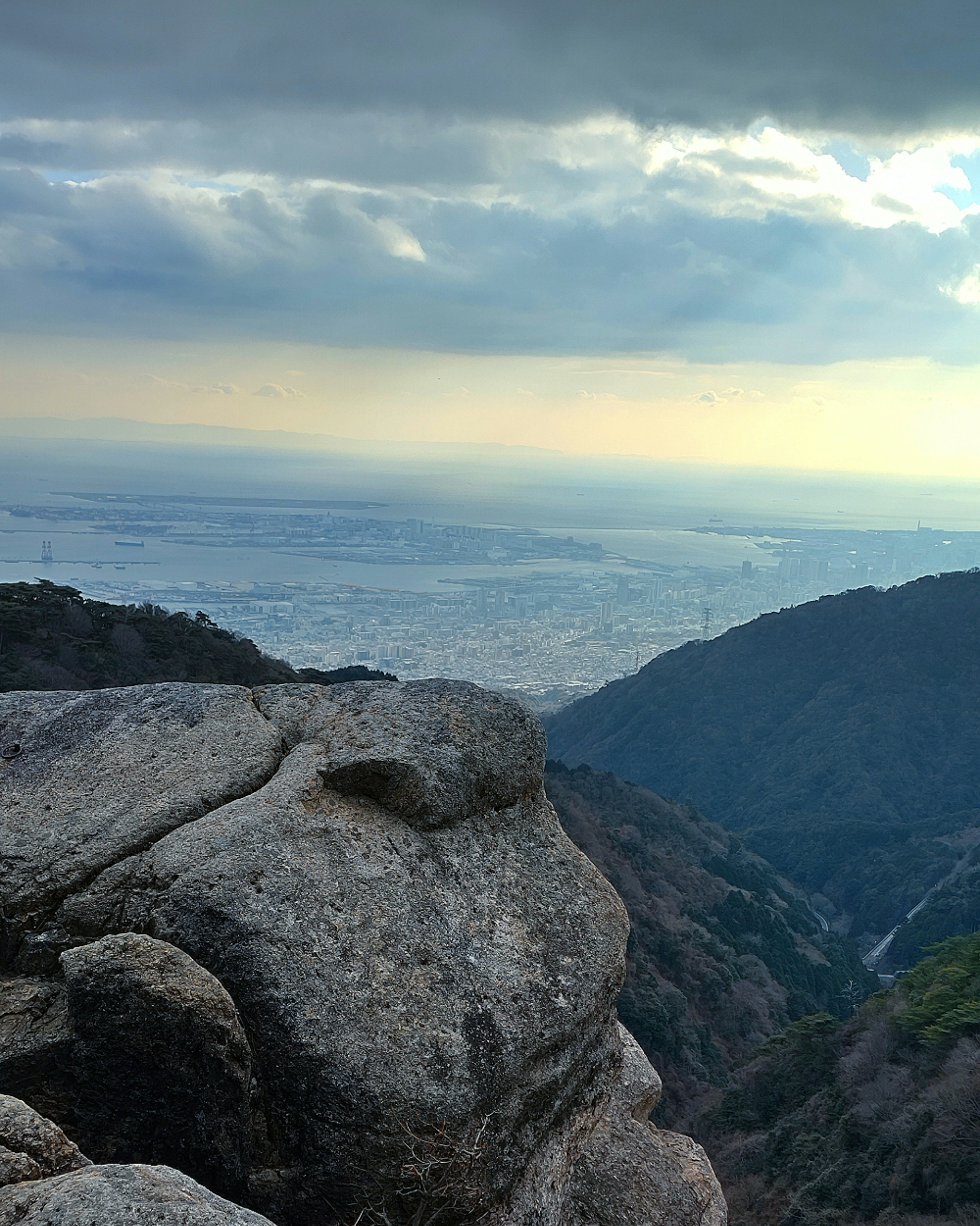 Scenic view from mountain peak featuring nearby rocks and distant city skyline