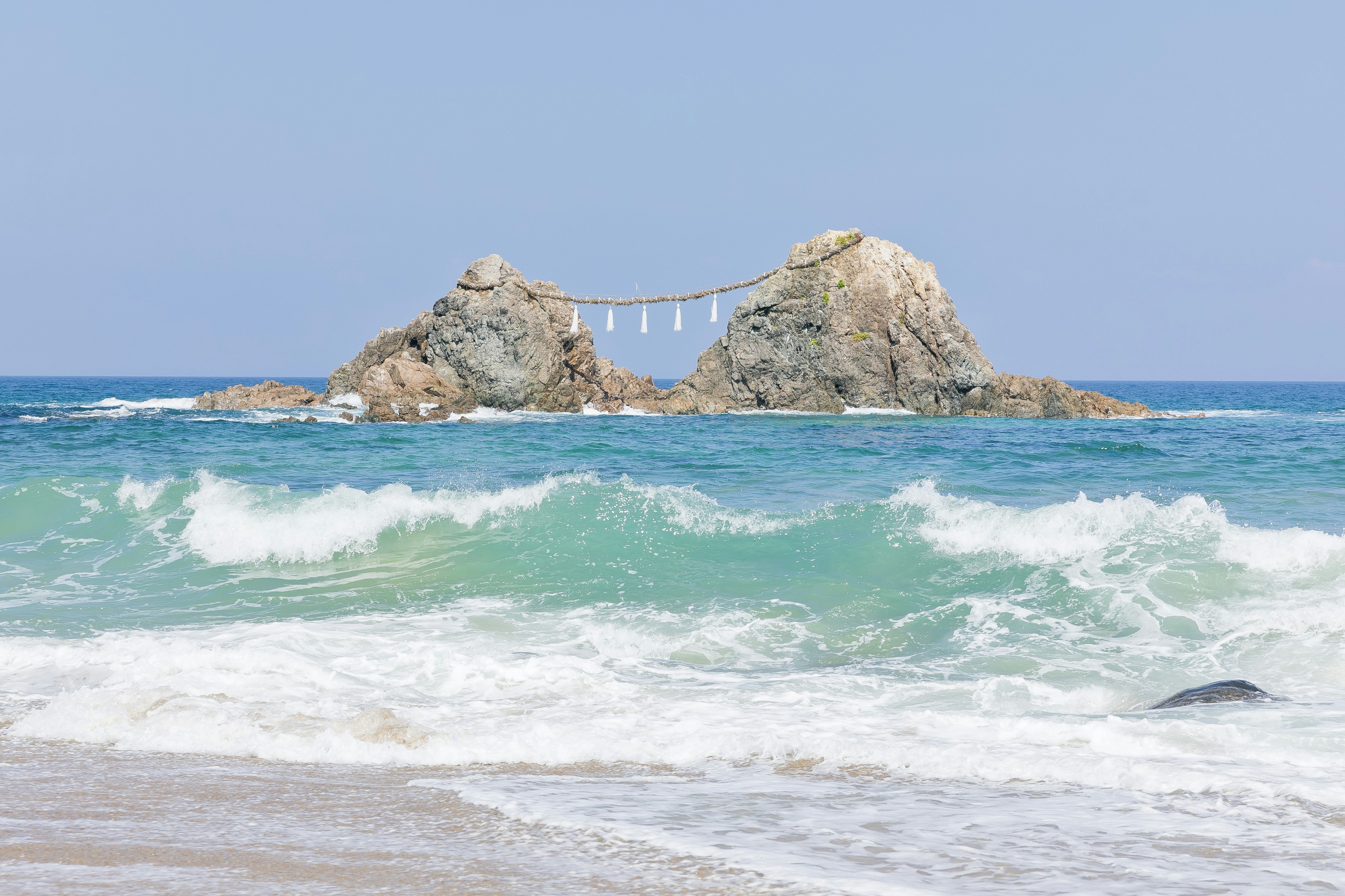 Malereische Aussicht auf blaue Ozeanwellen, die an eine felsige Küste schlagen, mit einer Brücke zwischen zwei Felsen