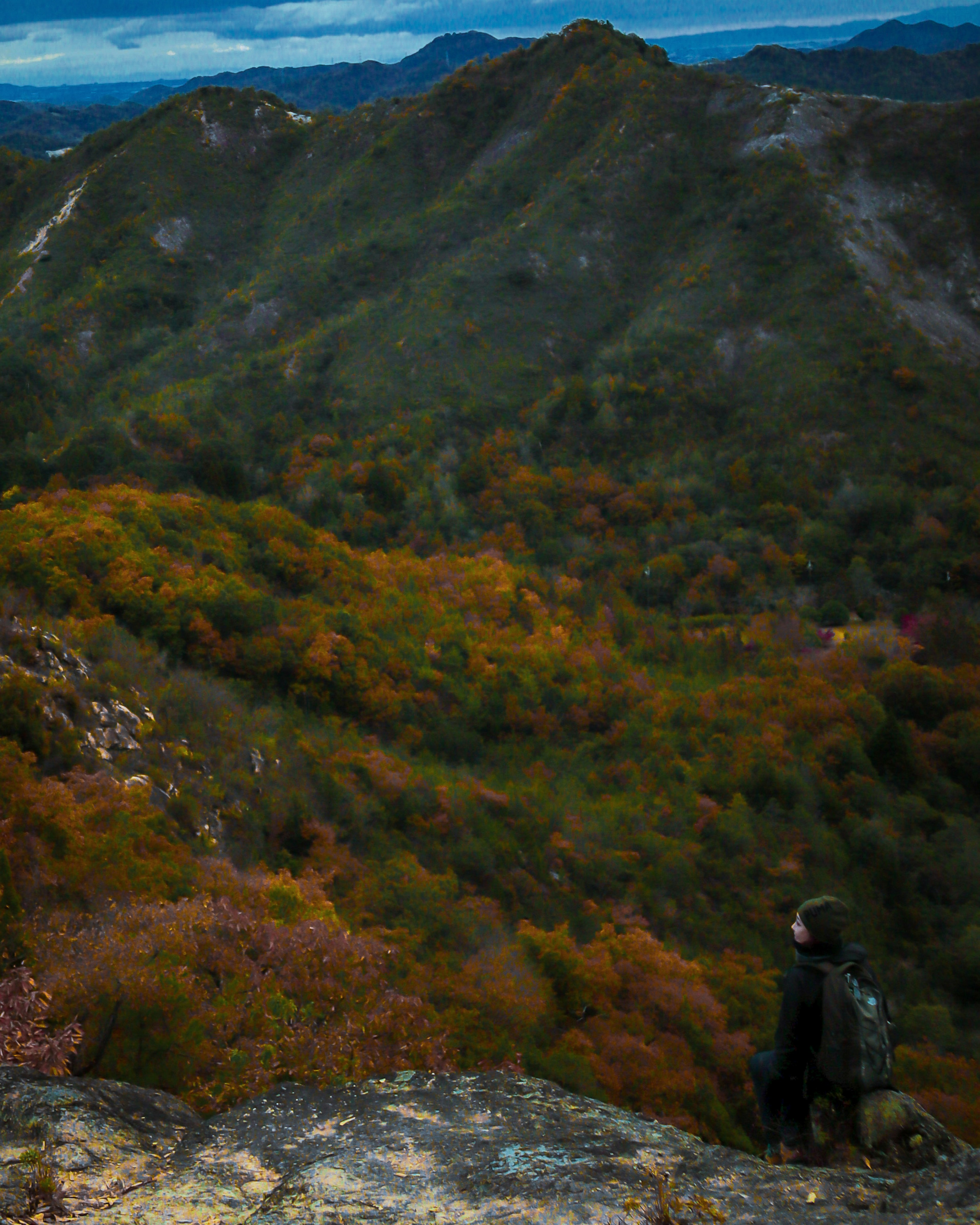 Hiker sitting on a mountain peak overlooking a beautiful autumn landscape