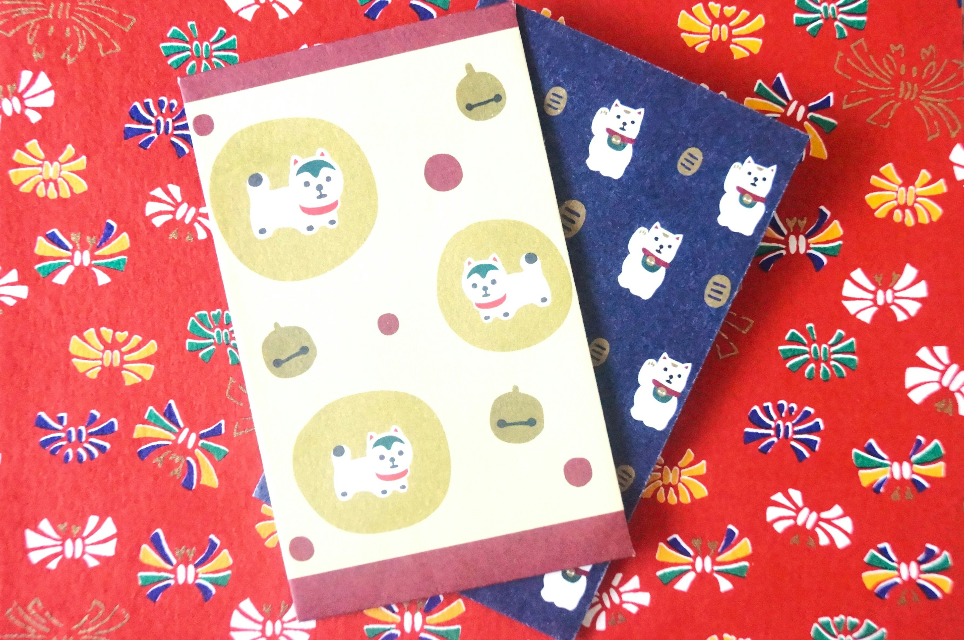 Two notebooks with colorful designs placed on a red background featuring cat illustrations and decorative patterns