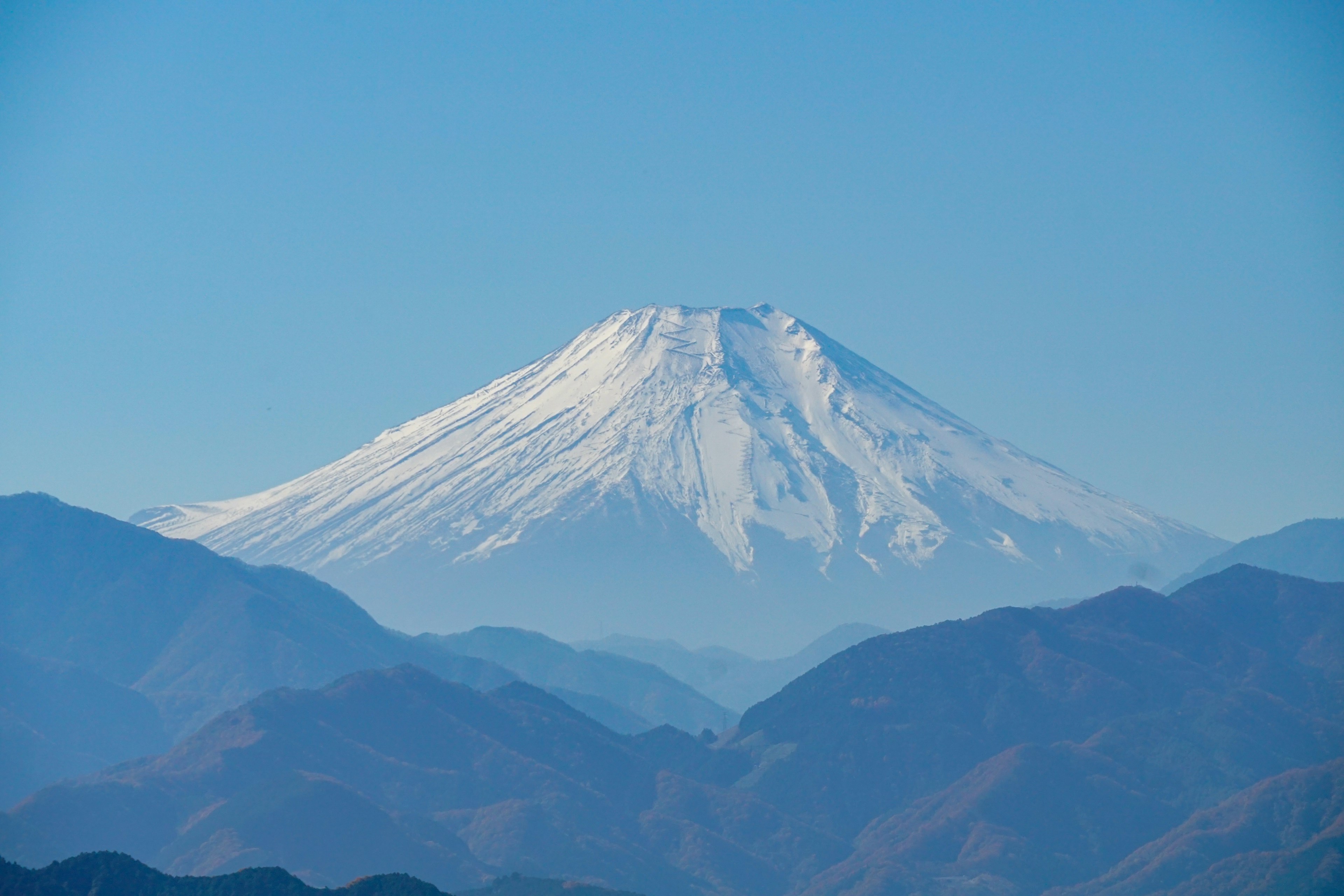 富士山の雪に覆われた壮大な姿が青空と山々の背景に映える