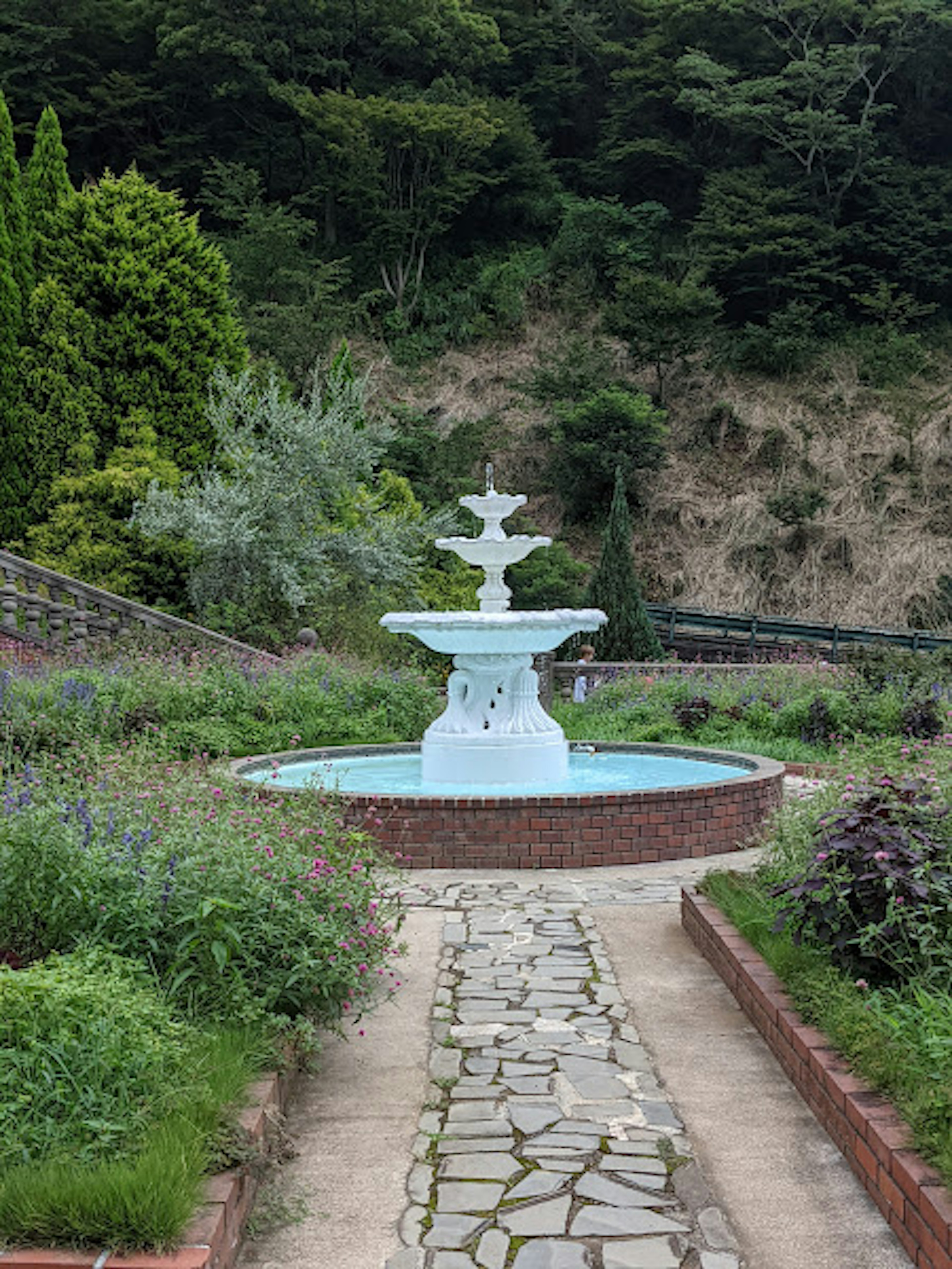 公園の中央にある白い噴水と周囲の緑豊かな植物