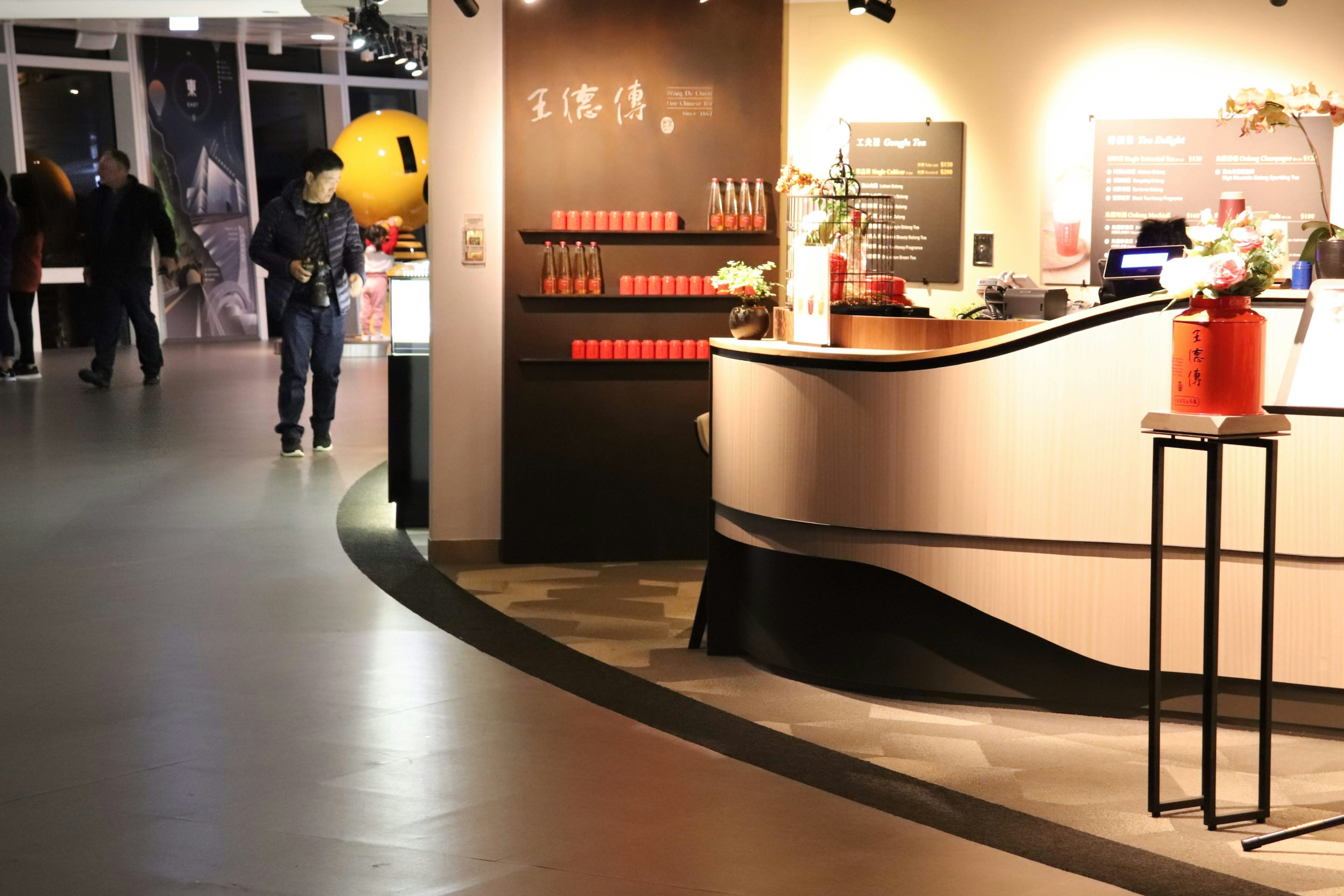 Modern reception area with a counter displaying red items and people walking in the background