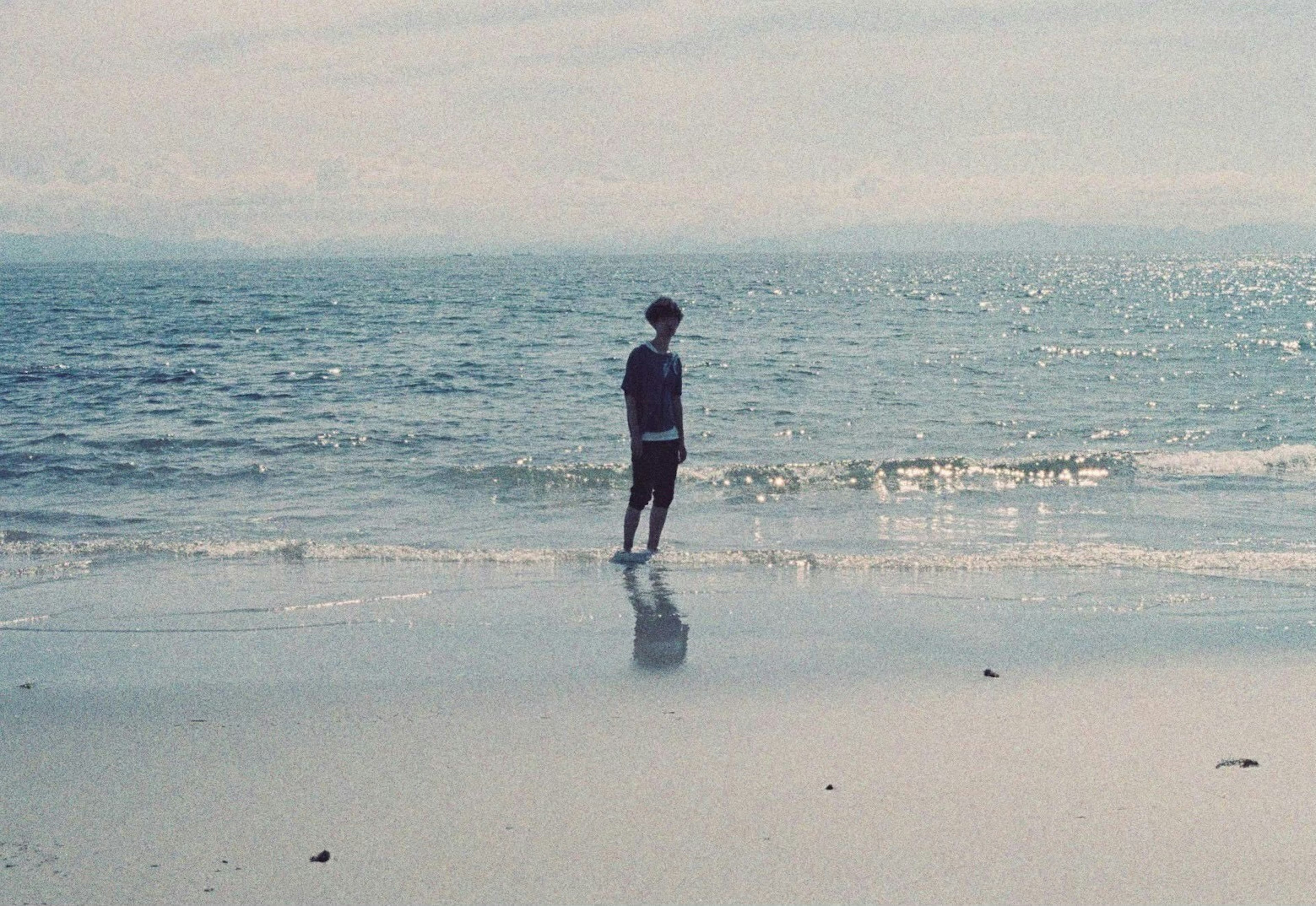 Person standing by the beach with gentle waves