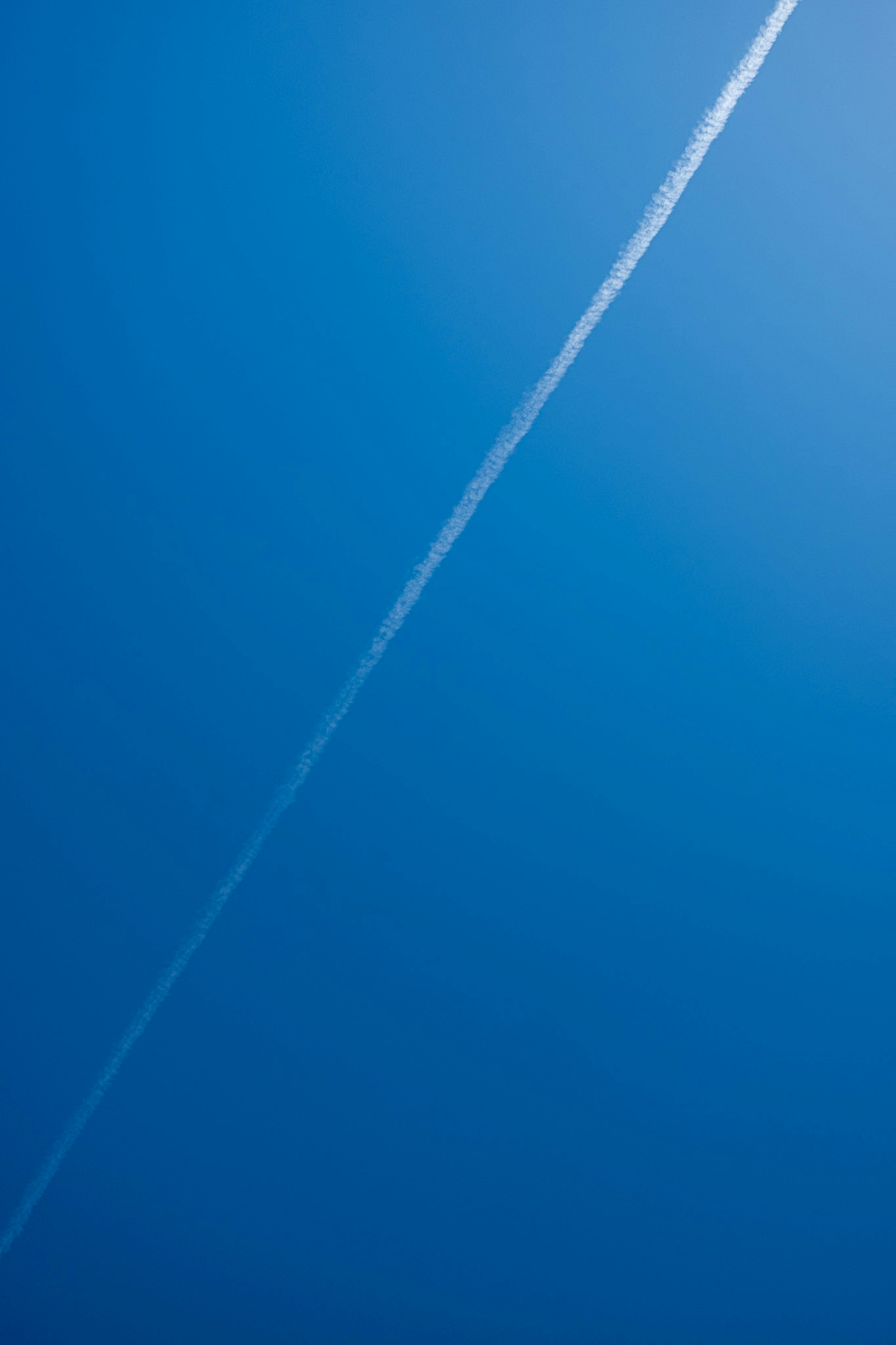 A white contrail forming a straight line in a clear blue sky