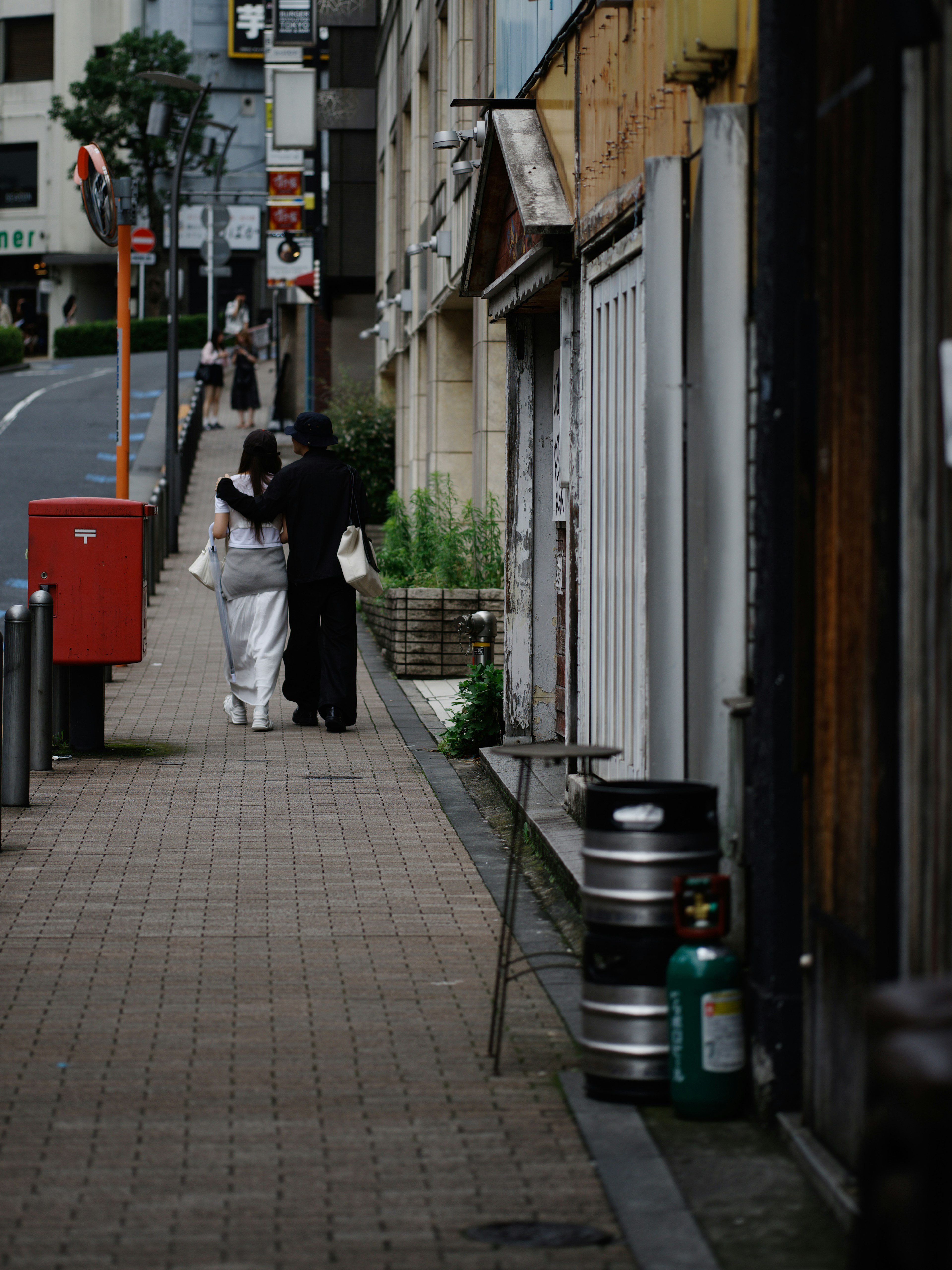 白い着物を着た女性と黒い衣装の男性が歩く街の風景