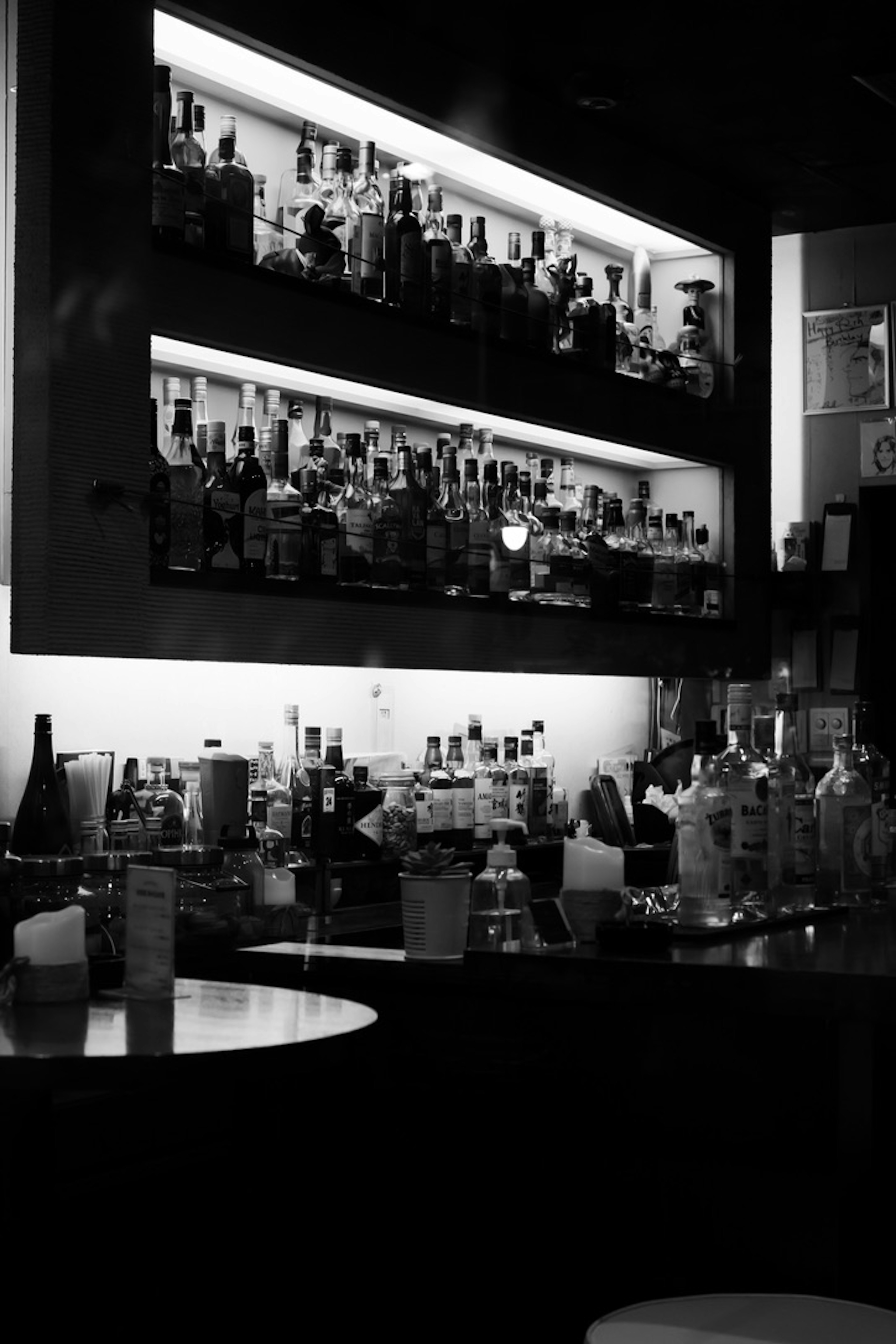 Black and white photo of a bar shelf filled with various bottles and cocktail glasses