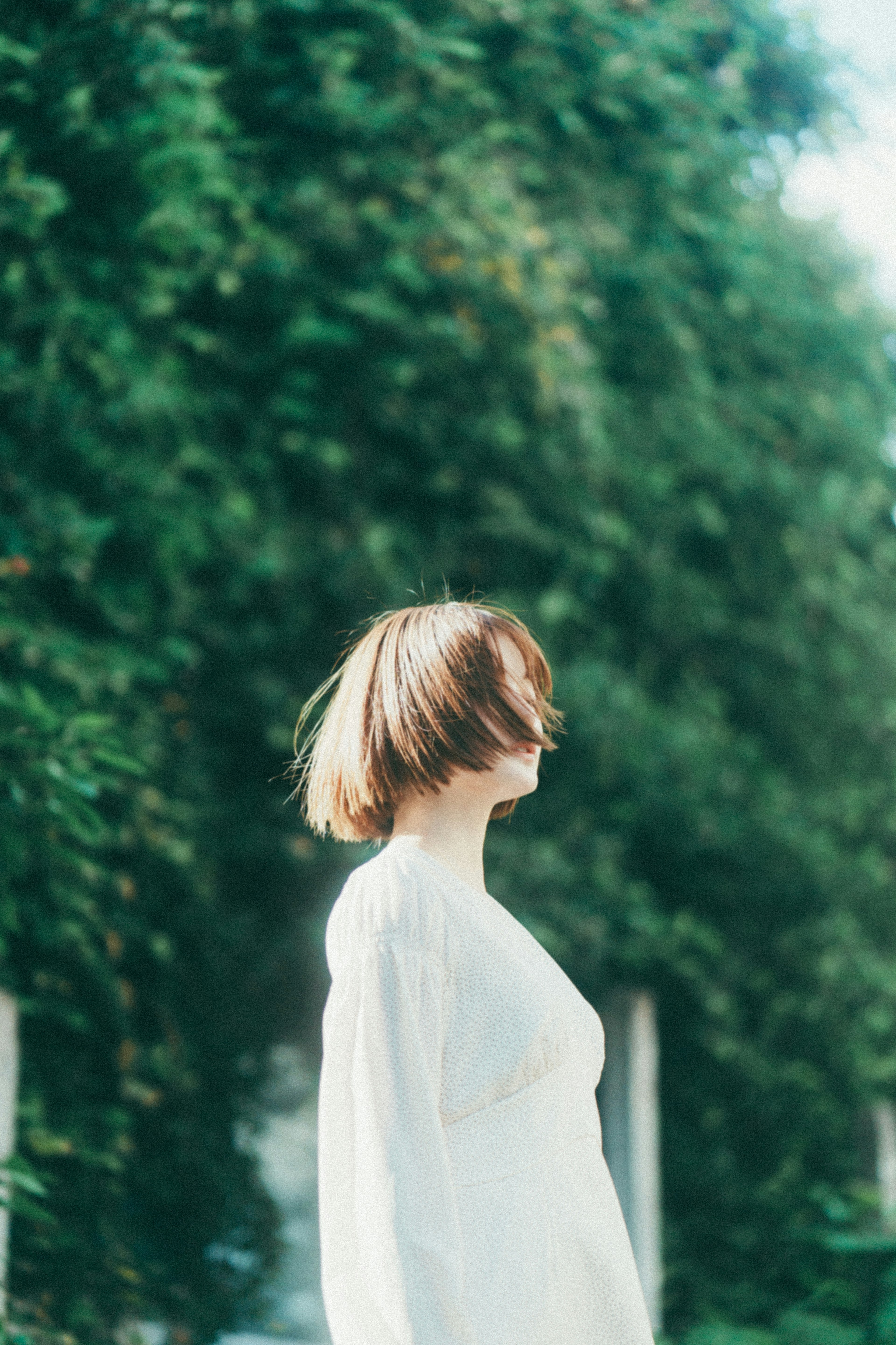 A woman in a white outfit with short hair swaying against a backdrop of green trees