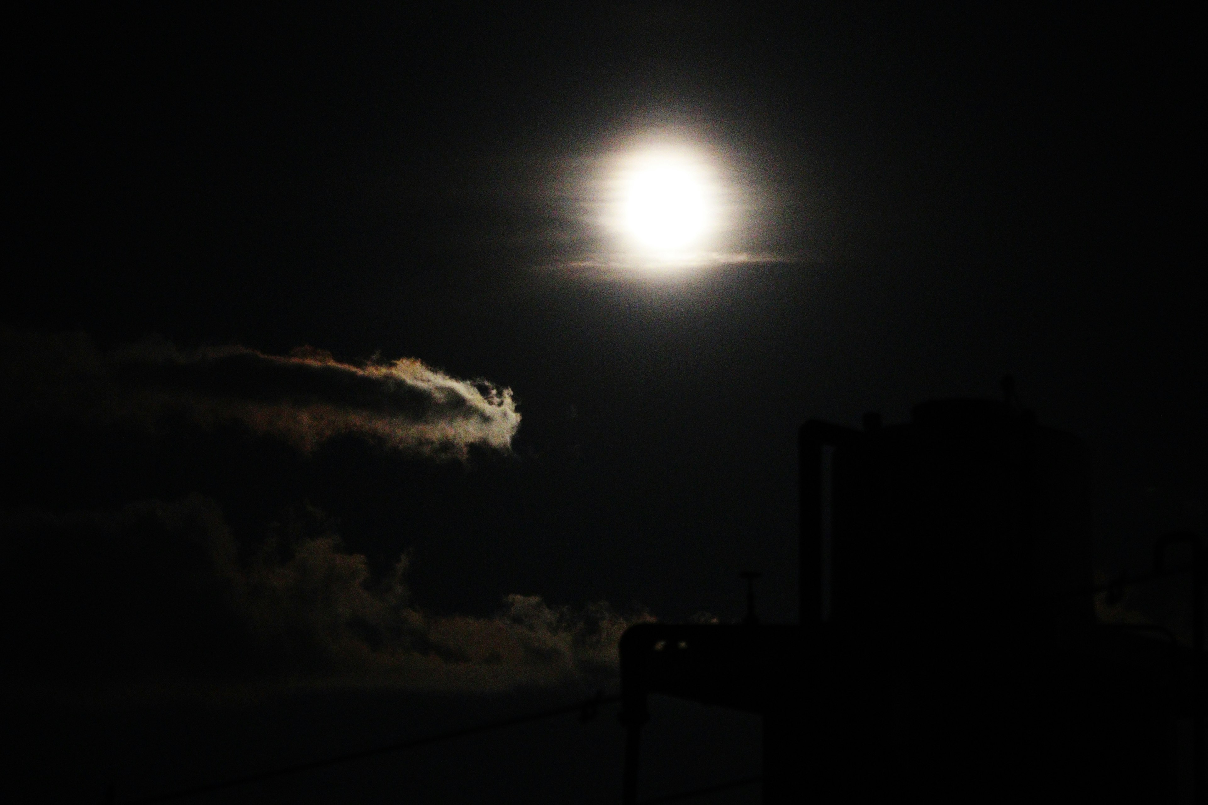 Luna llena brillante en un cielo oscuro con silueta de nubes y estructuras