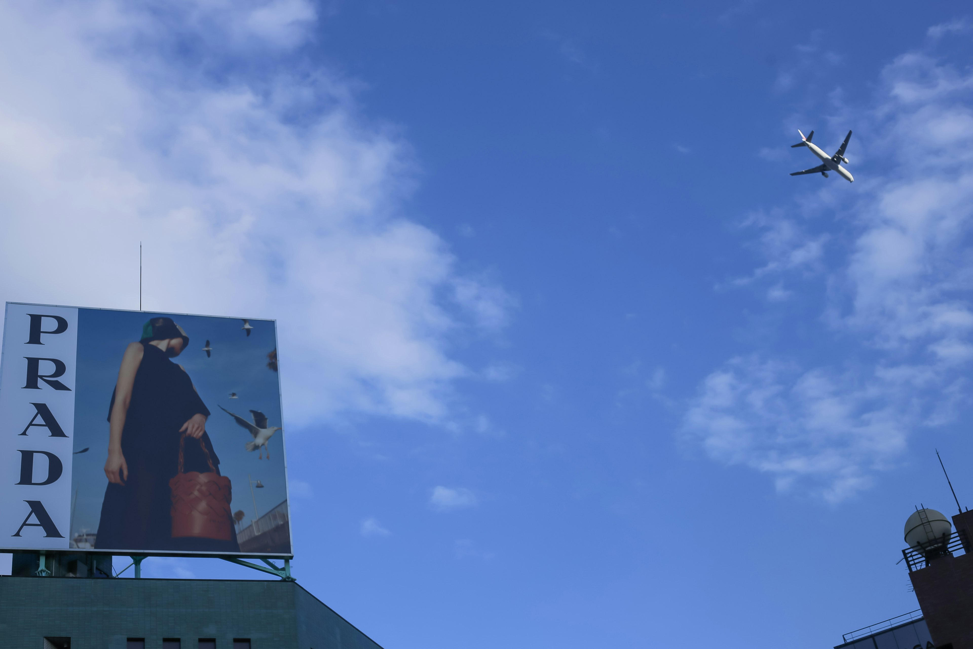 青空の下にあるプラダの広告看板と飛行機