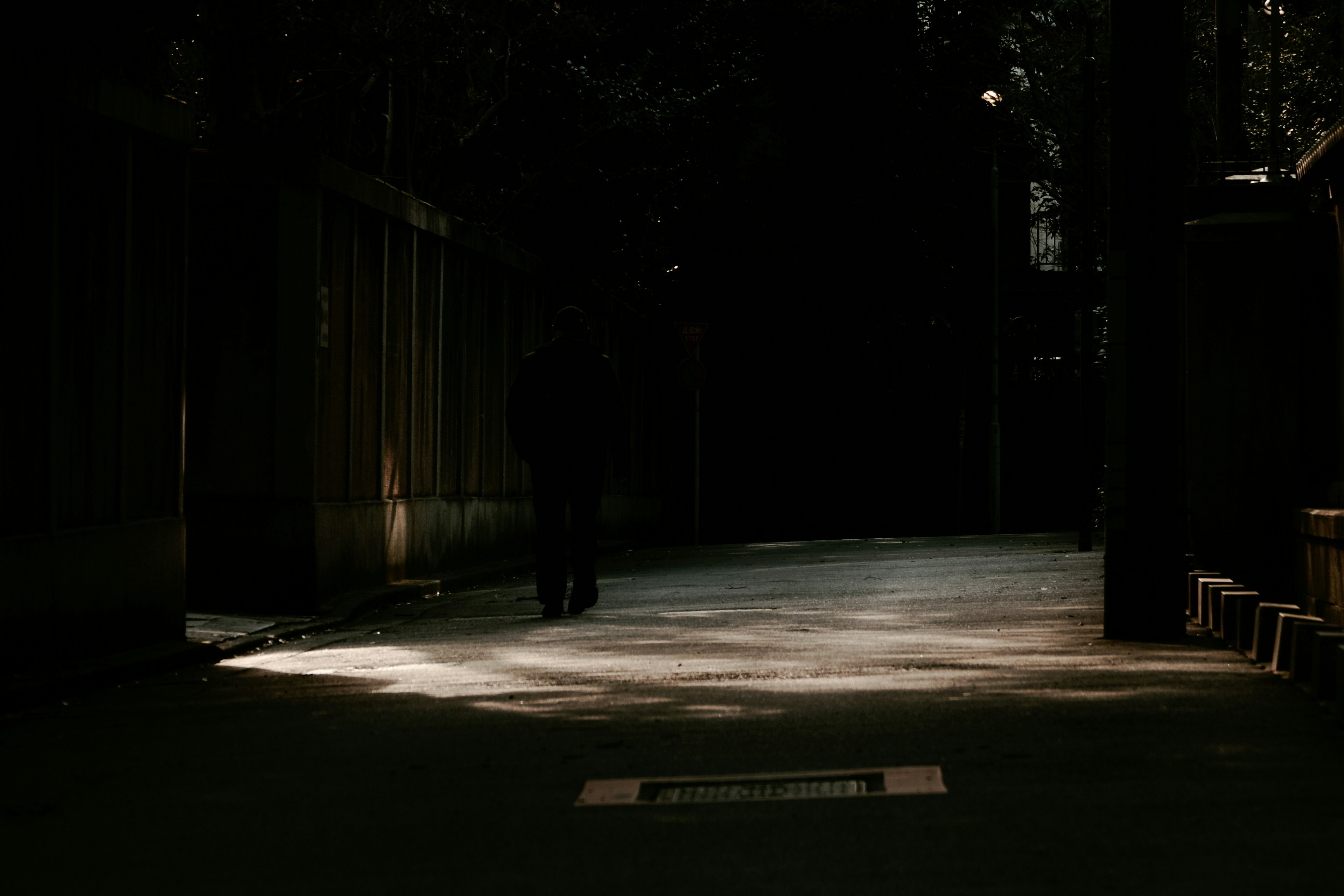 Silhouette d'une personne marchant dans une ruelle faiblement éclairée avec un contraste de lumière