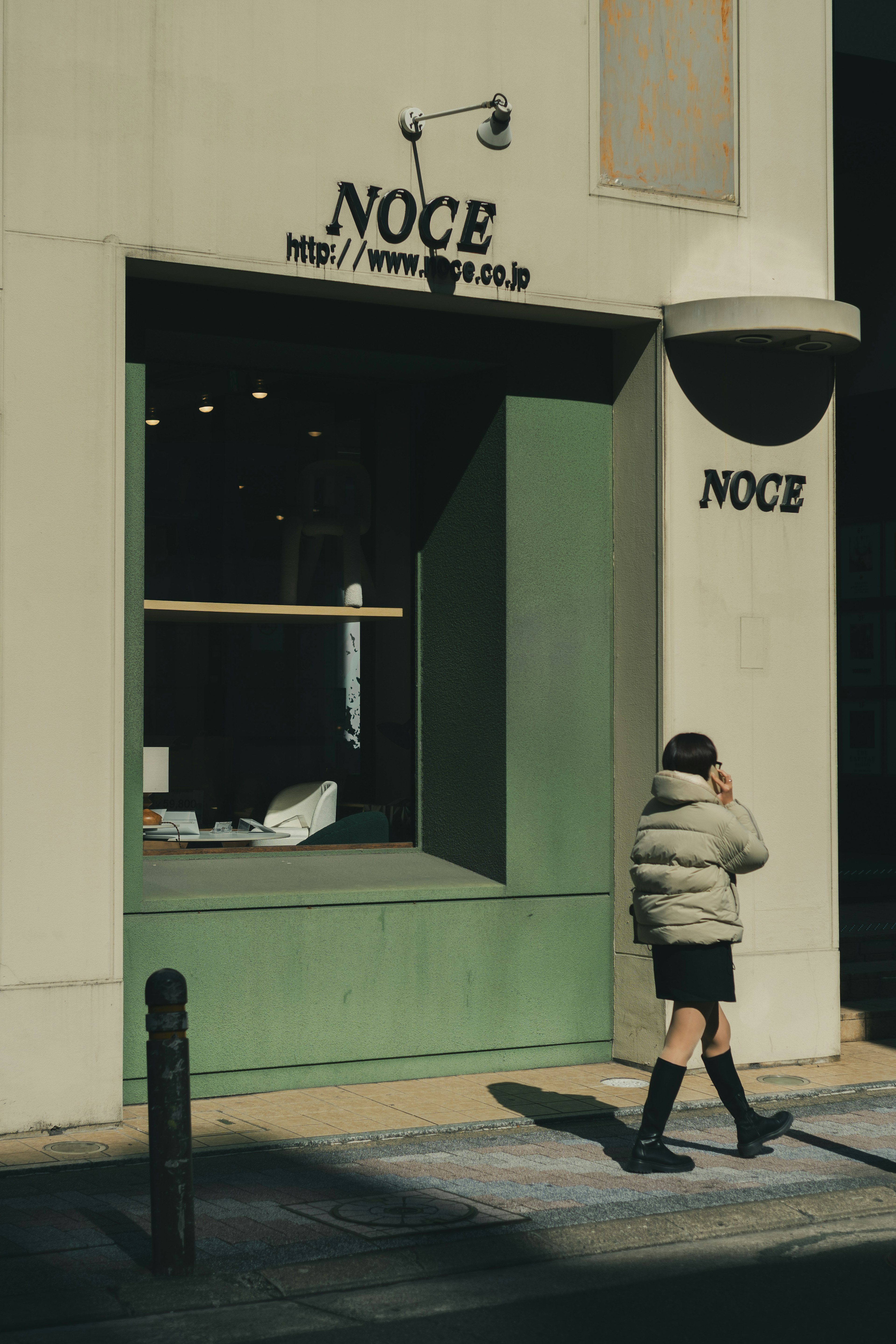 Exterior of NOCE store featuring a person walking and green window