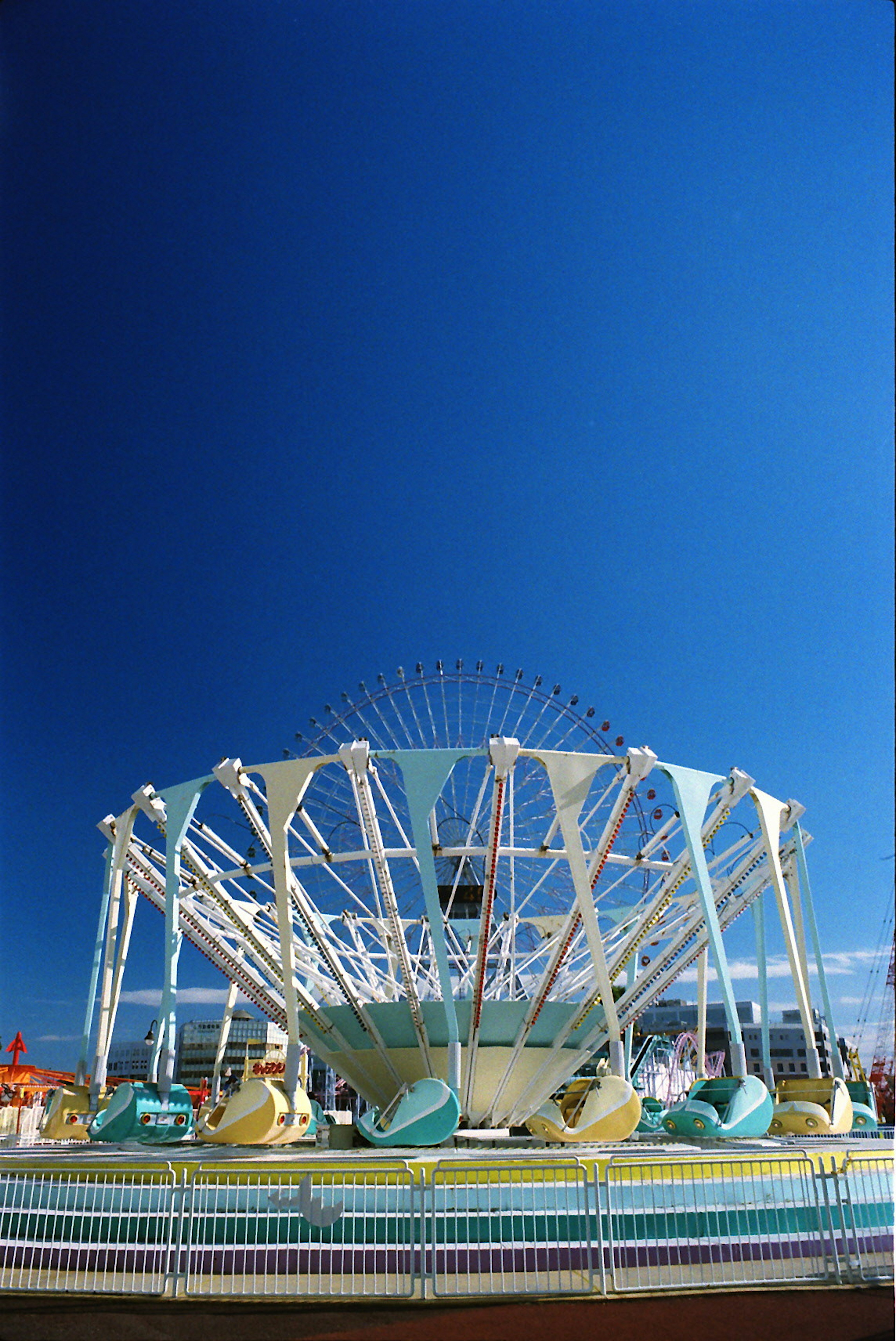 Foto di un carosello in un parco divertimenti sotto un cielo blu con un design bianco e azzurro e giostre colorate