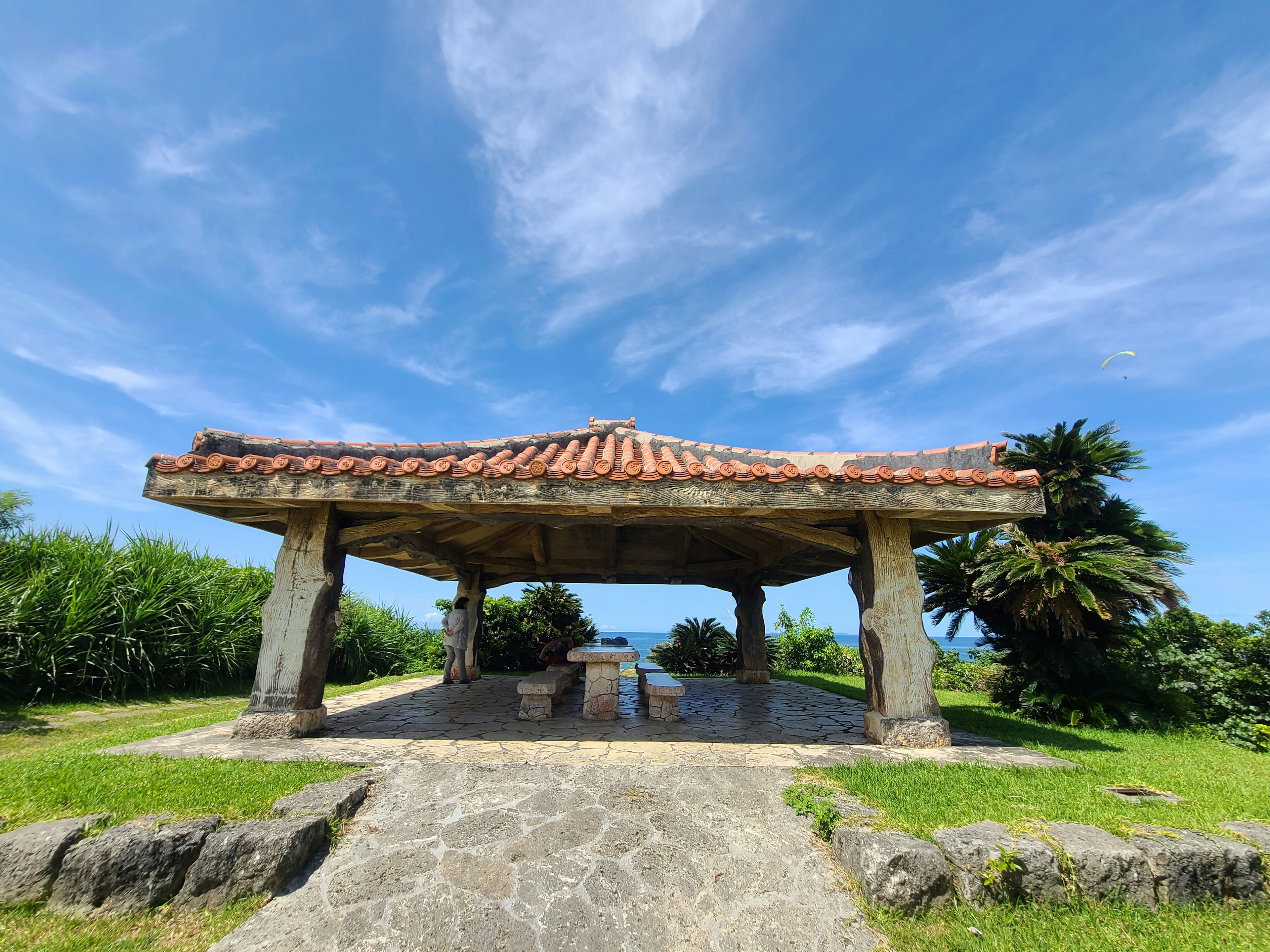 Pavilion with a tiled roof under a blue sky surrounded by green grass