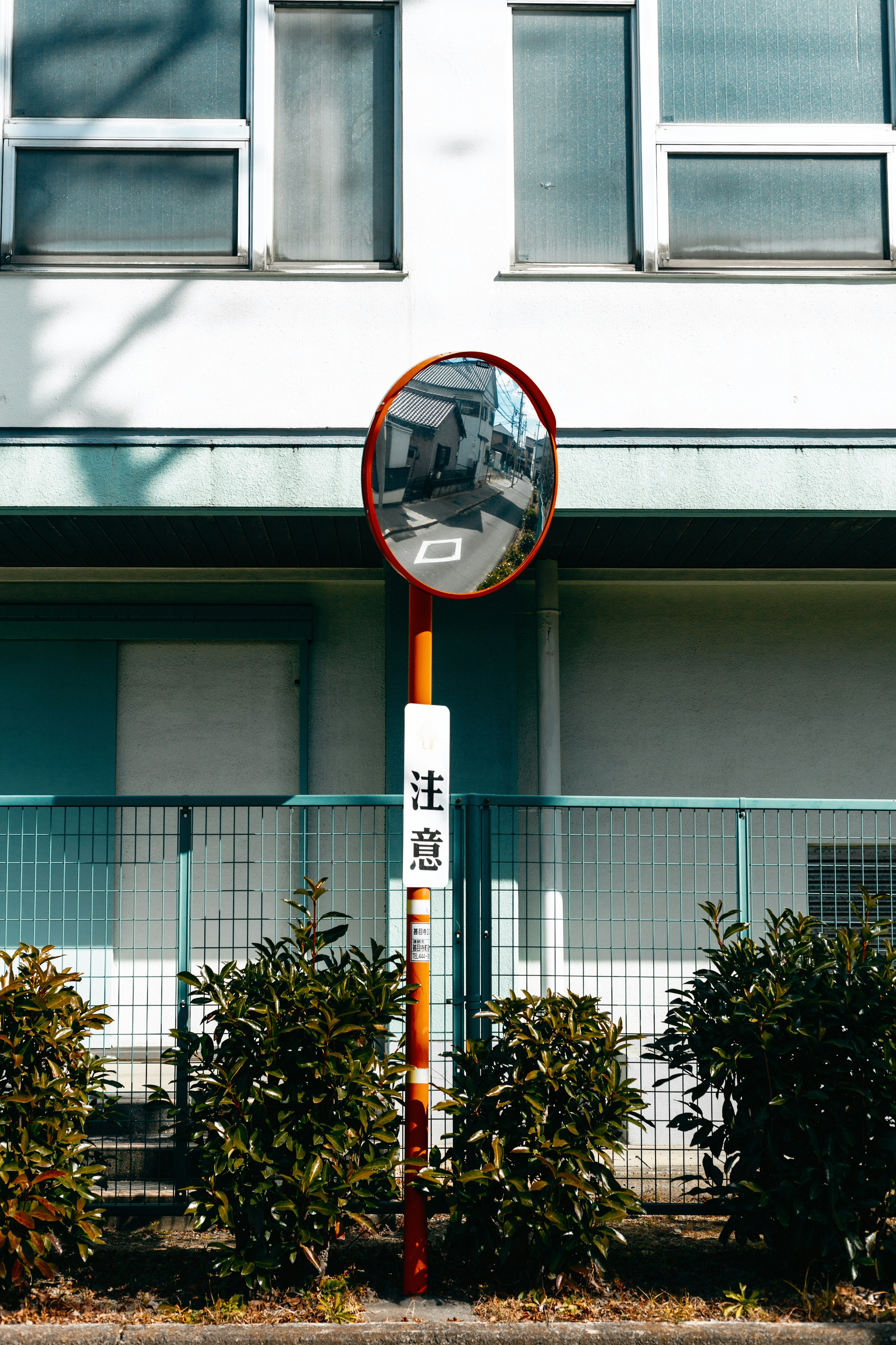 Round mirror in front of a building with green shrubs