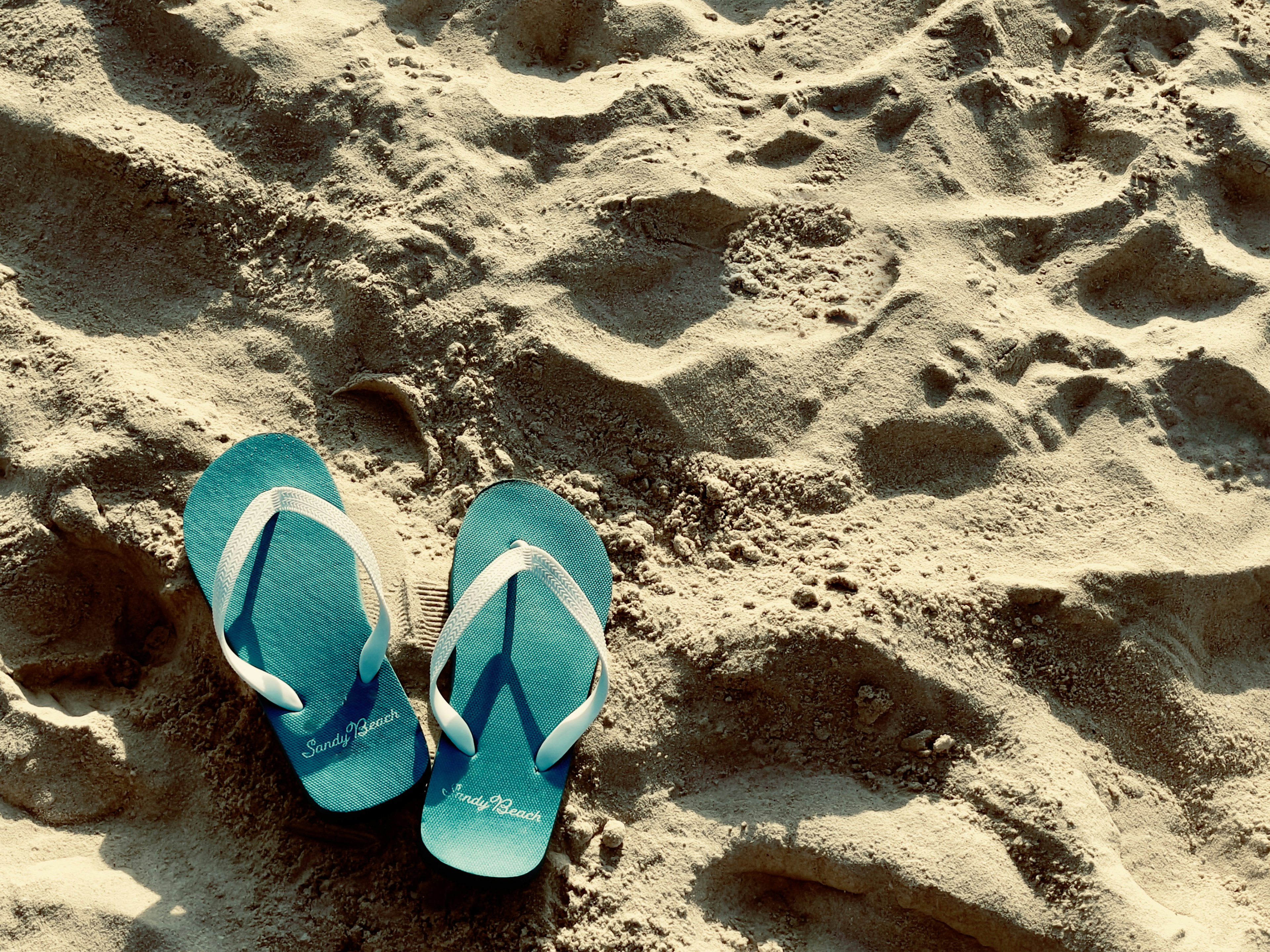 Blue flip-flops resting on sandy beach