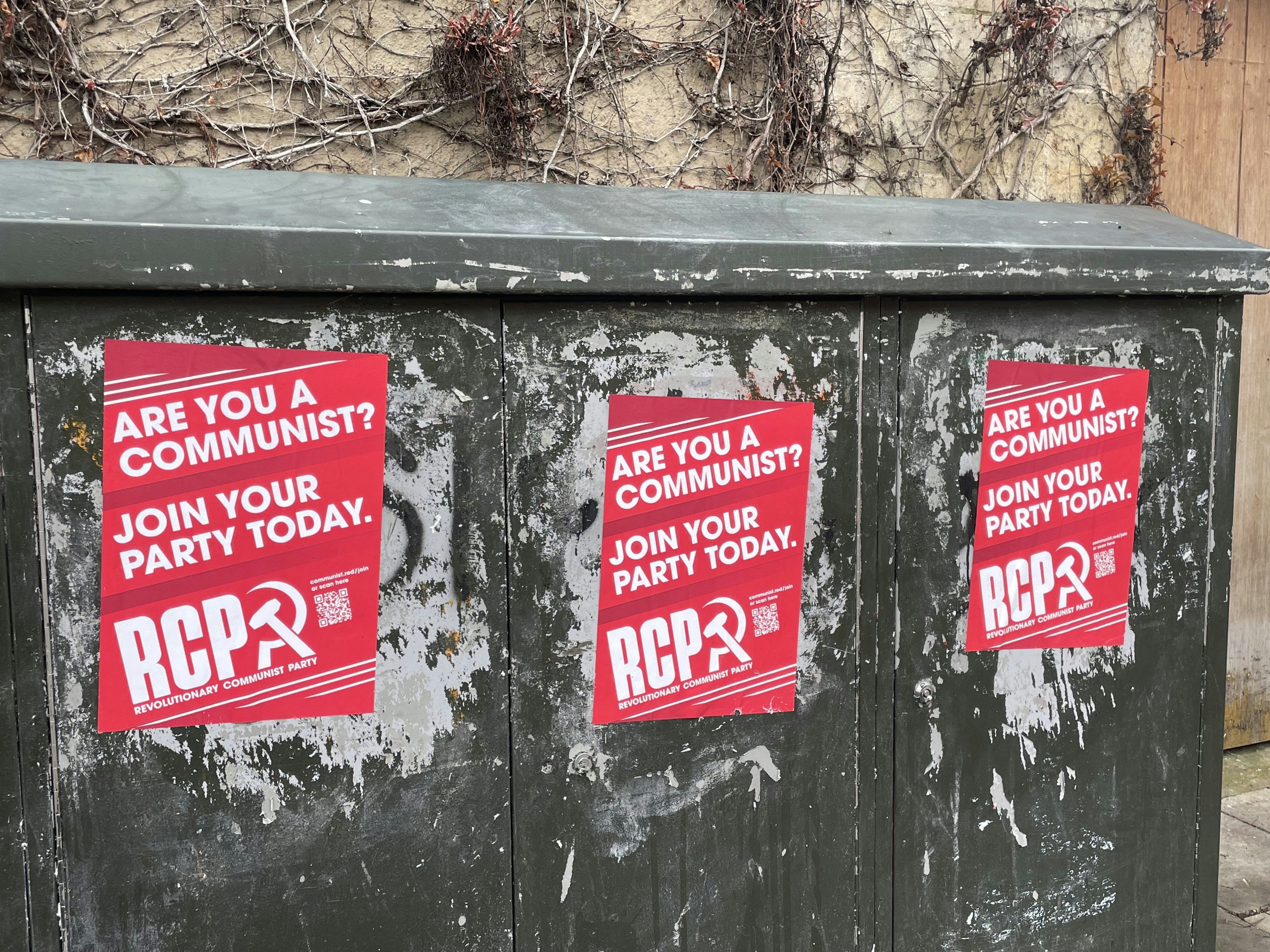 Grüner Versorgungskasten mit roten Plakaten zur Mitgliedschaft in einer Kommunistischen Partei