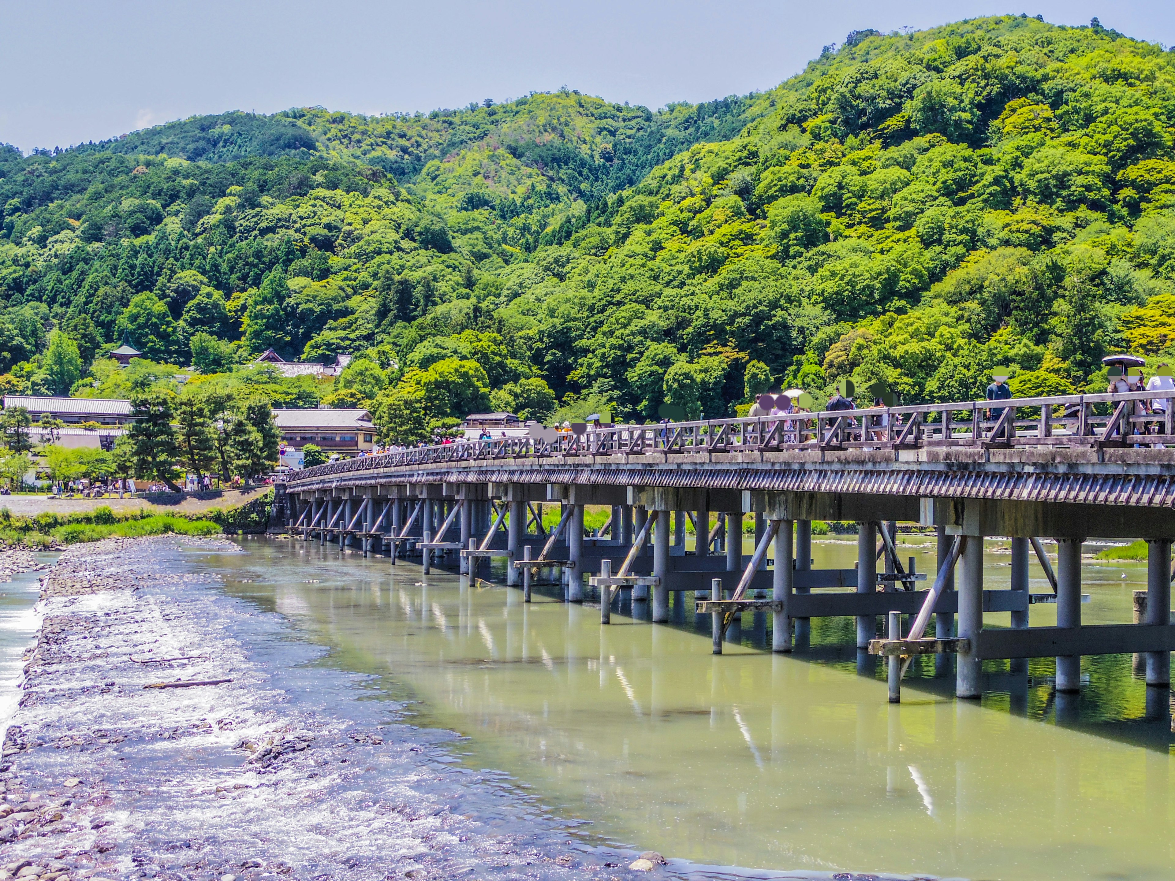 Jembatan kayu yang melintasi sungai dikelilingi bukit hijau