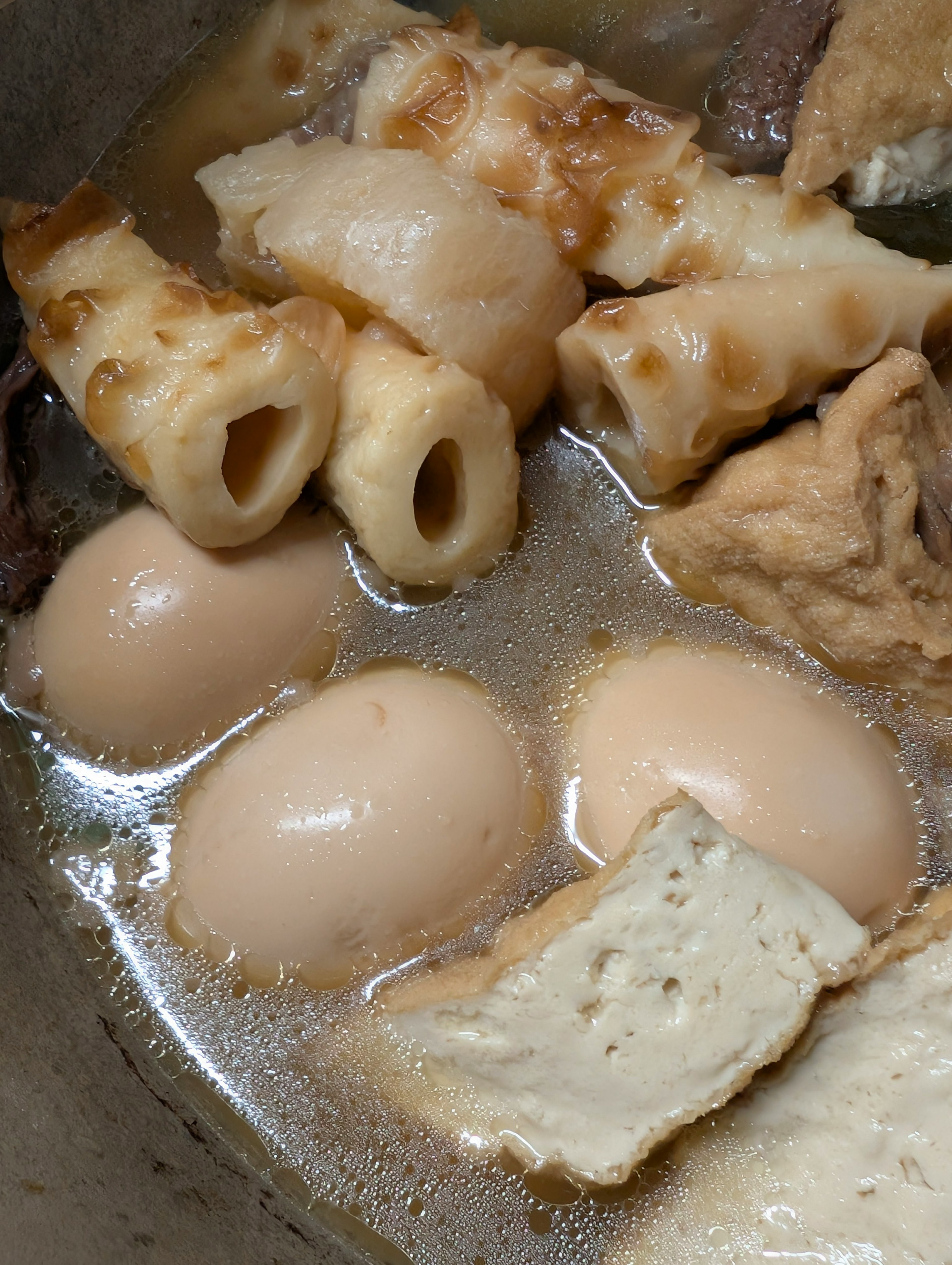 A pot of simmering soup with boiled eggs and various fish cakes