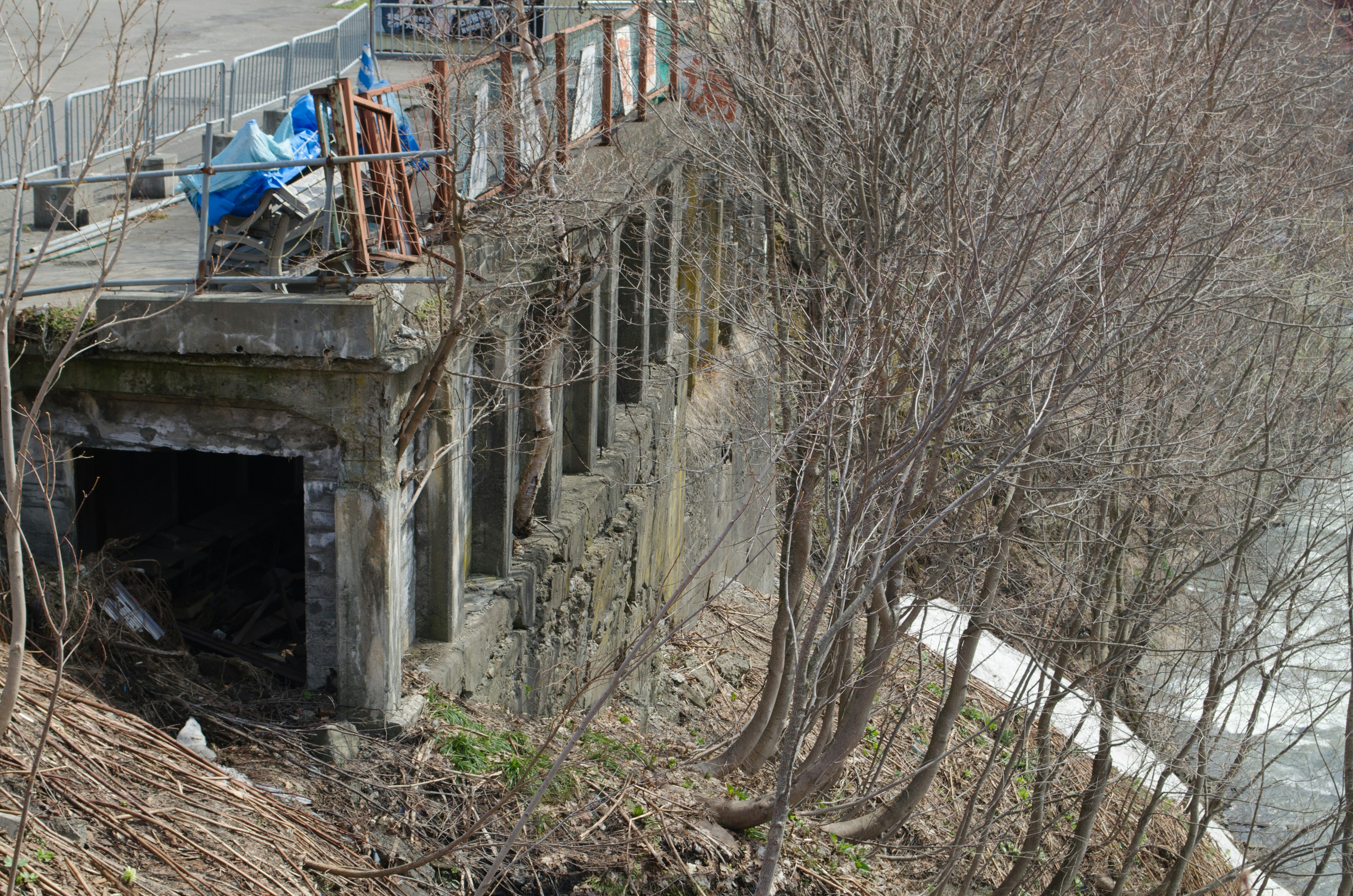 Abandoned concrete structure with bare trees and riverbank