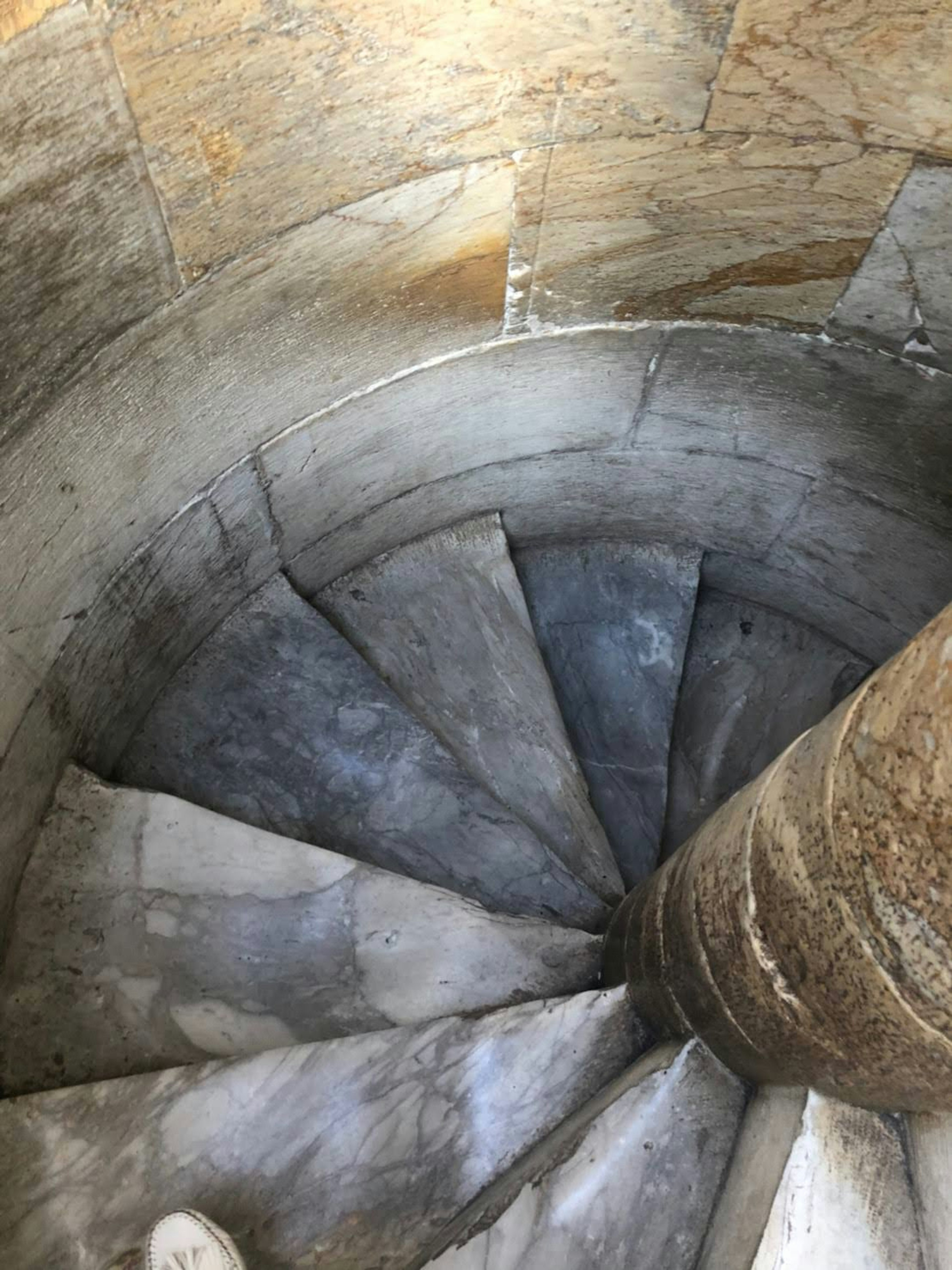 View from above of a spiral staircase with stone railing and smooth steps