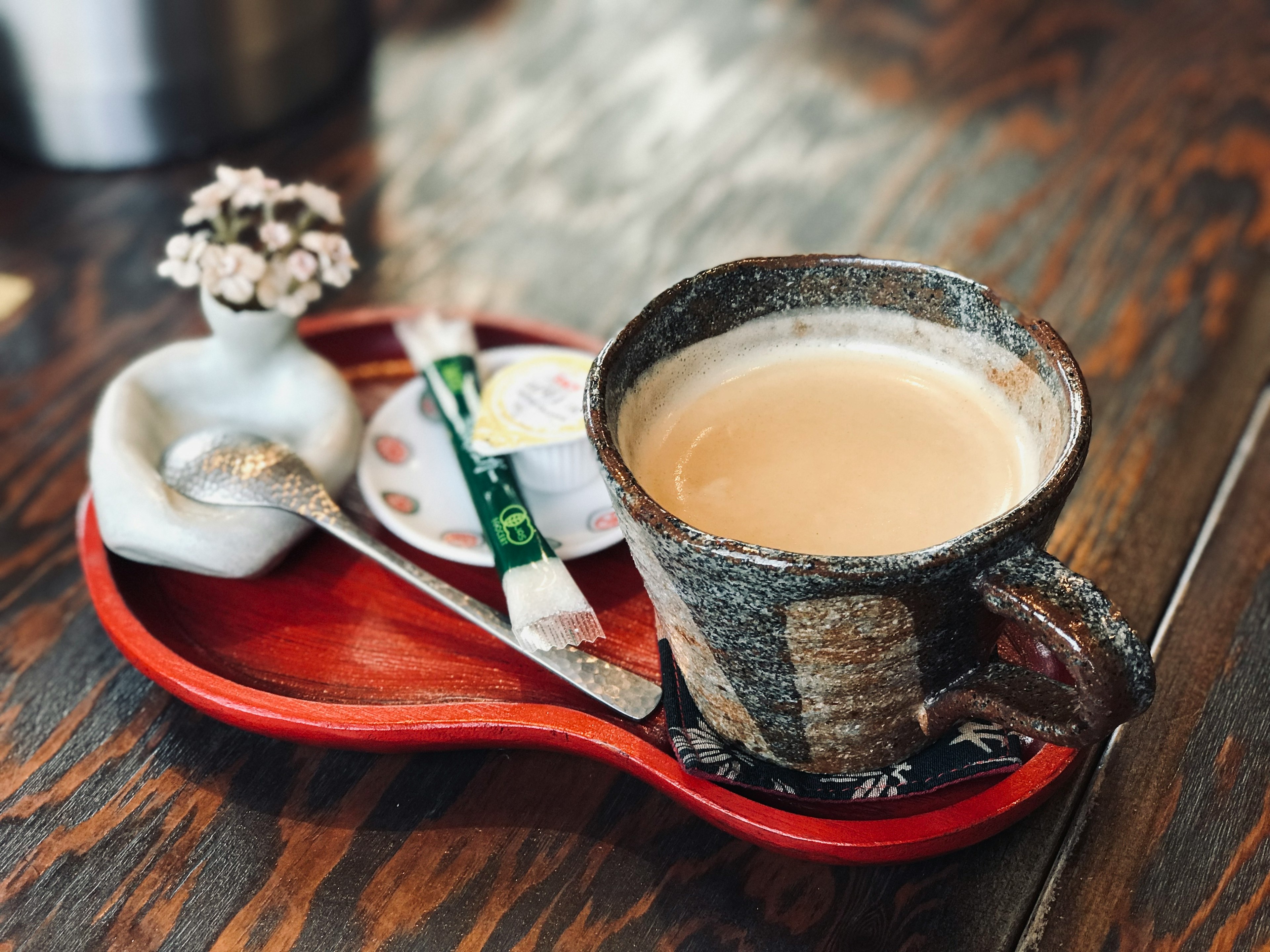 コーヒーが入った陶器のカップと小さな花瓶が乗ったトレイ