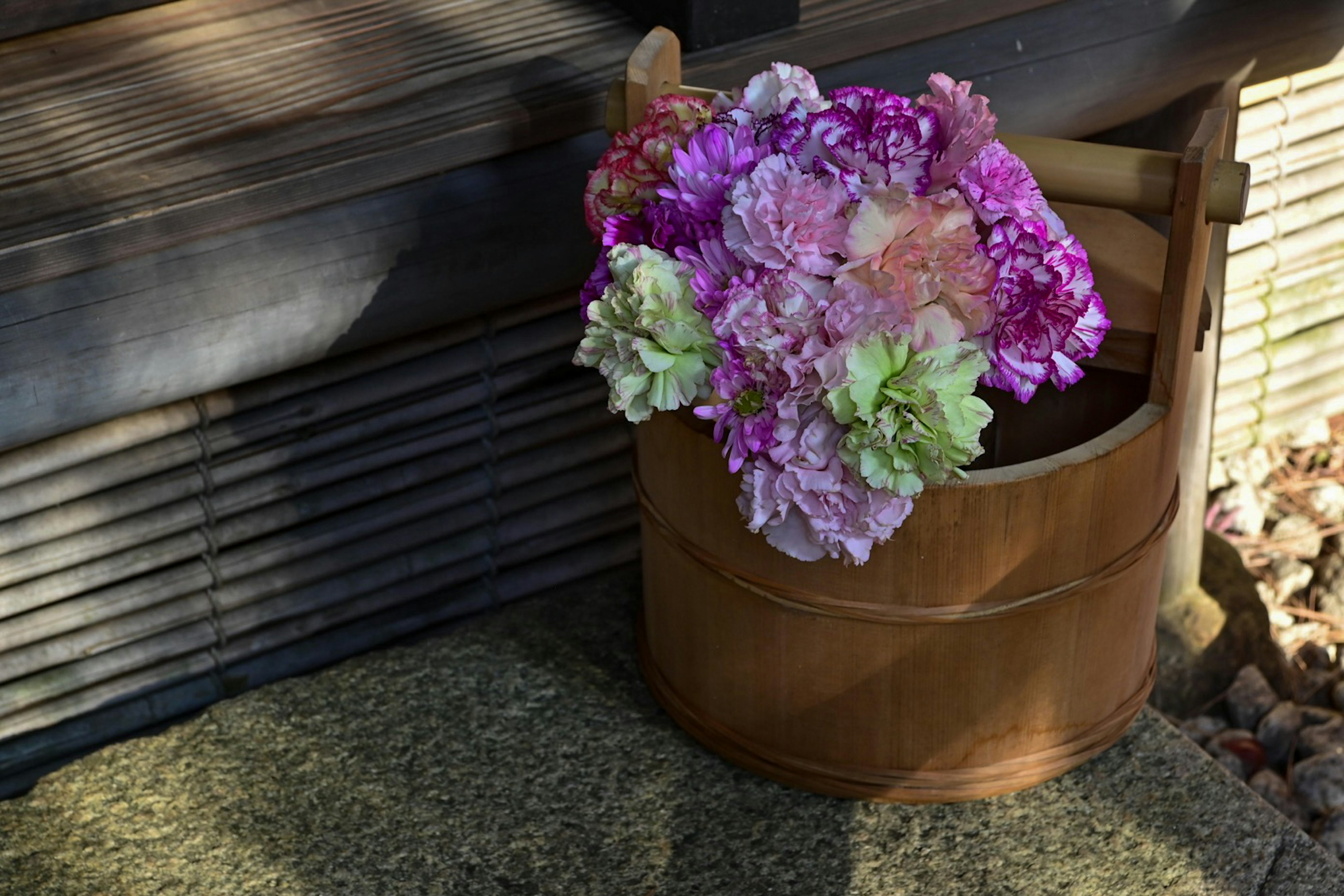 A wooden bucket filled with colorful flowers placed beside wooden flooring