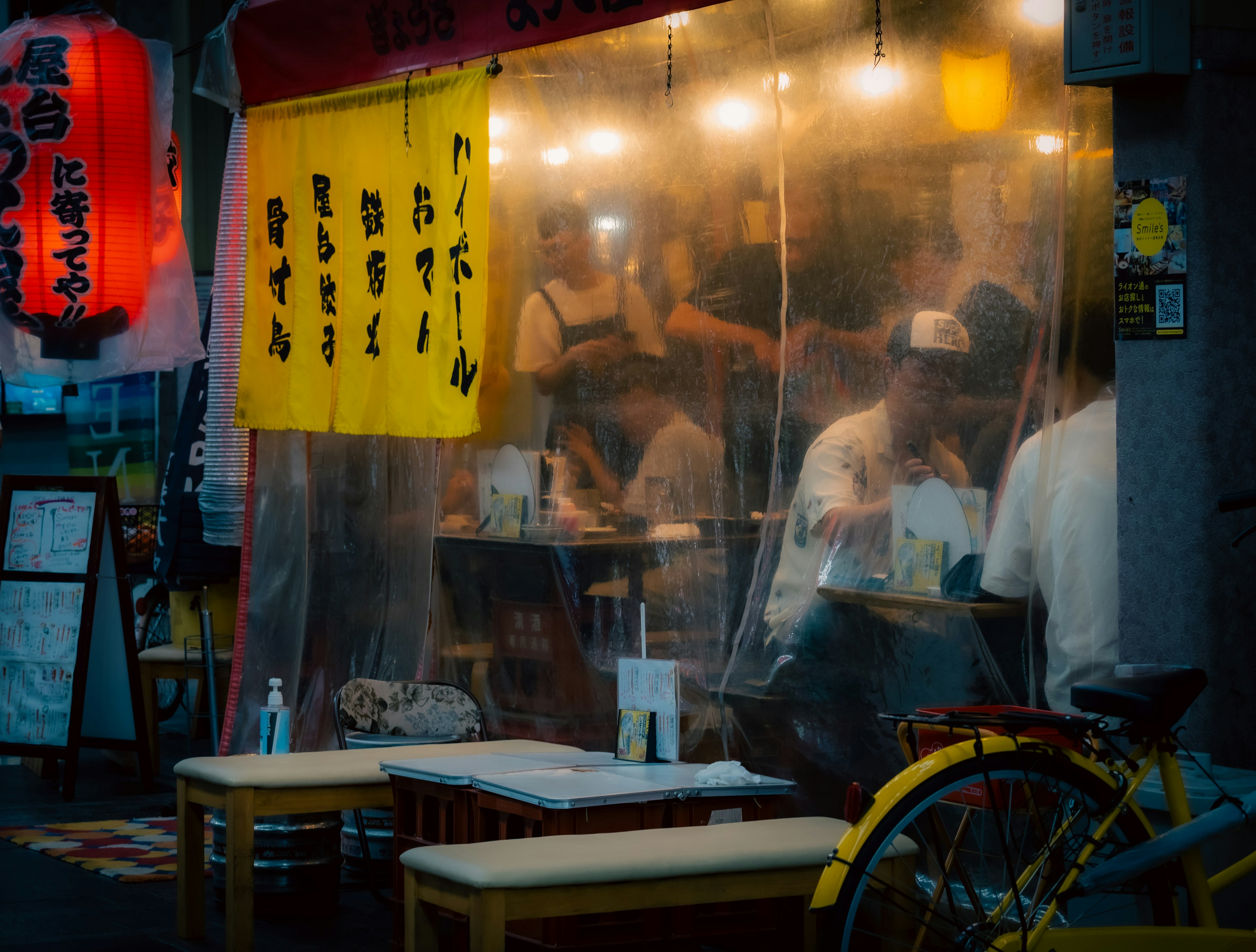 แผงขายอาหารข้างถนนพร้อมไฟสว่างและผู้คนที่นั่งกินข้างใน