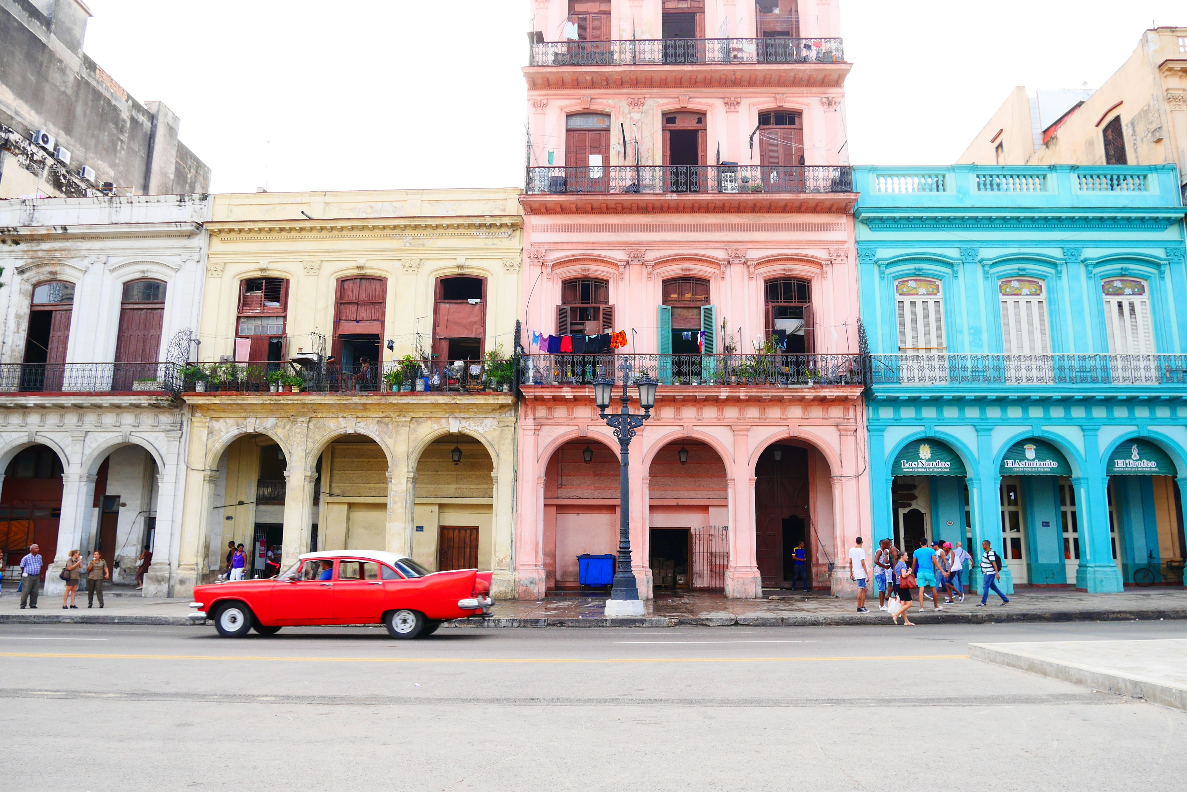 Edifici colorati lungo una strada dell'Avana Auto d'epoca rossa parcheggiata davanti