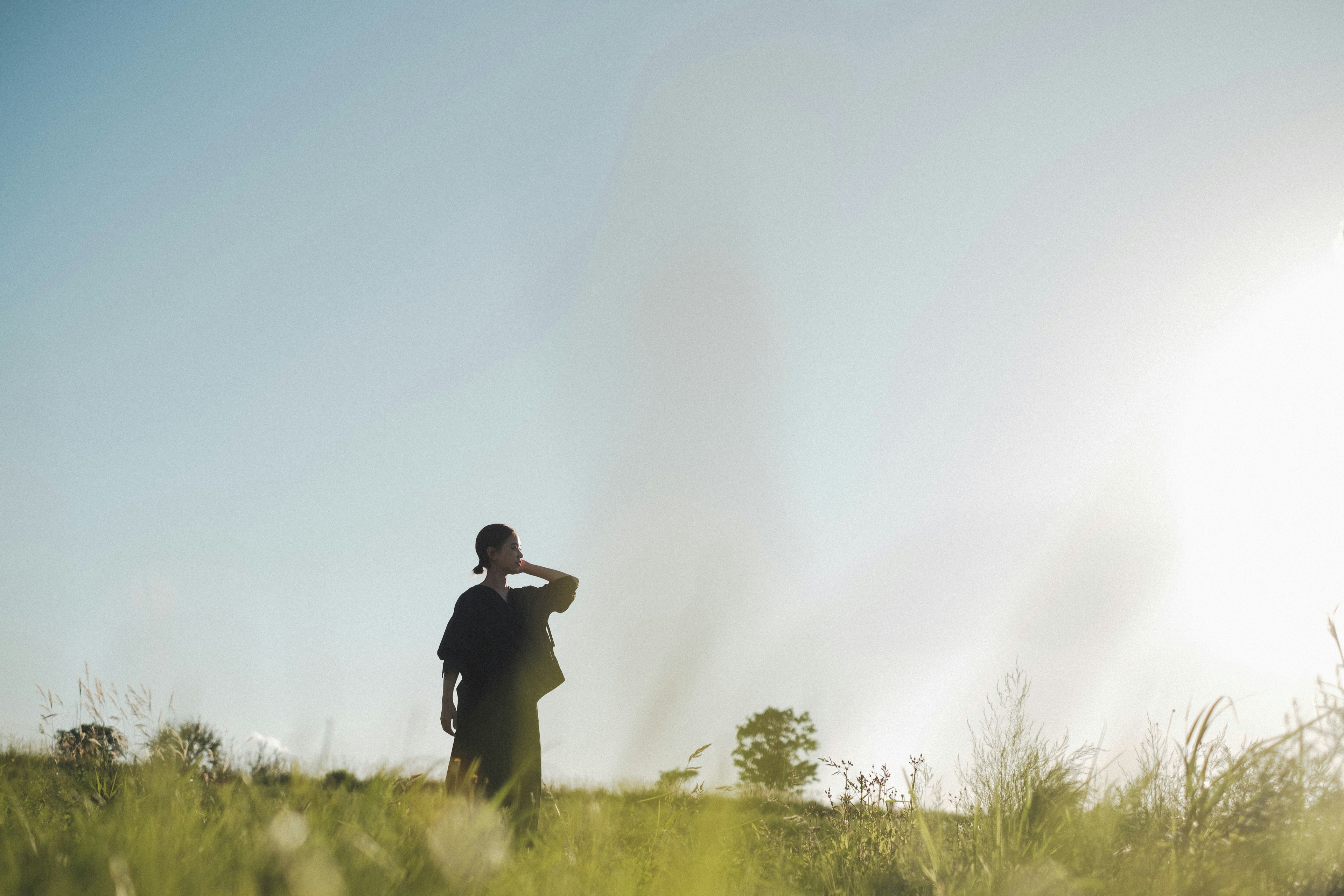 A person standing under a blue sky shielding their eyes