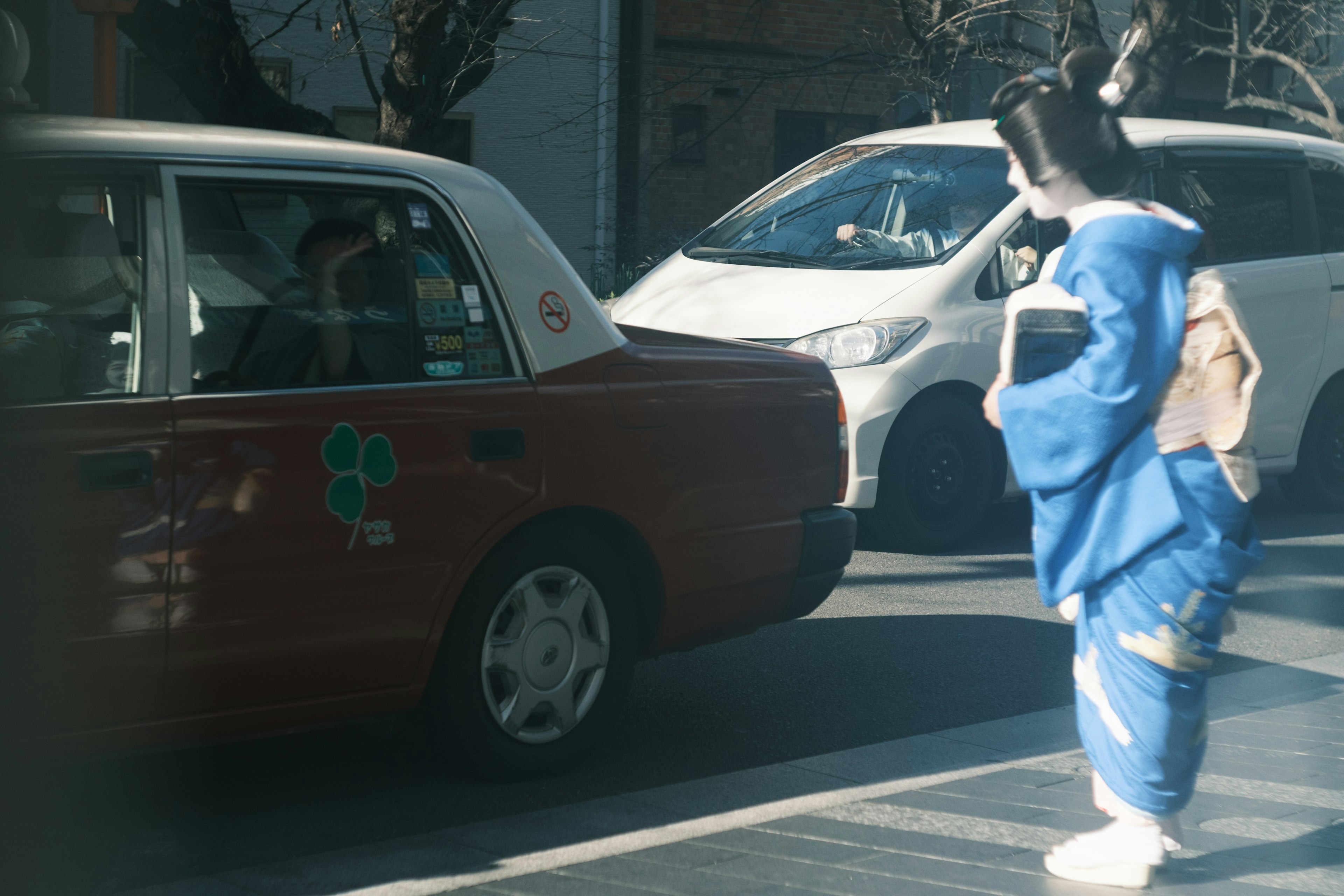 Eine Frau im blauen Kimono steht vor einem Taxi