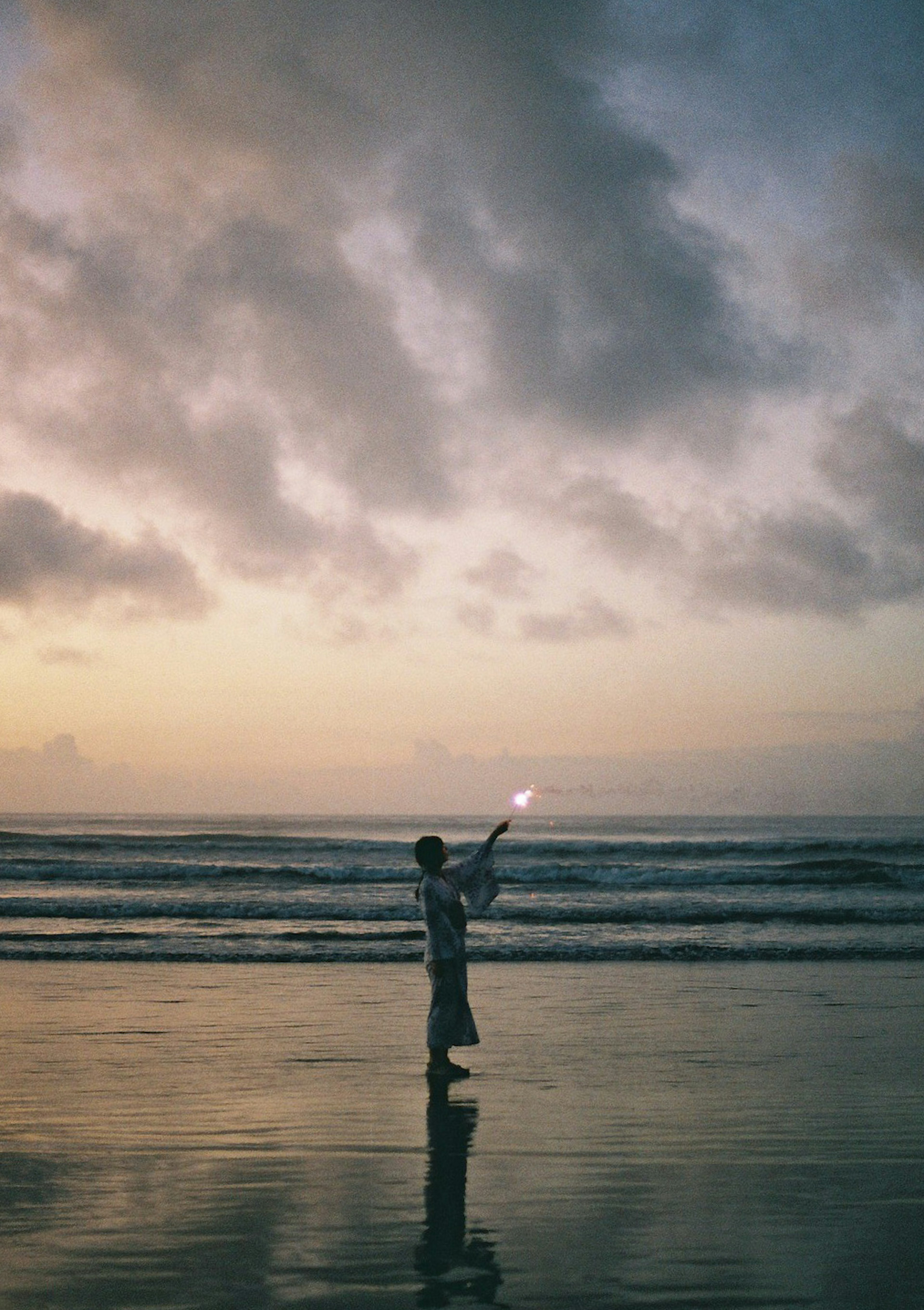 Siluet anak yang memegang kembang api di pantai saat matahari terbenam