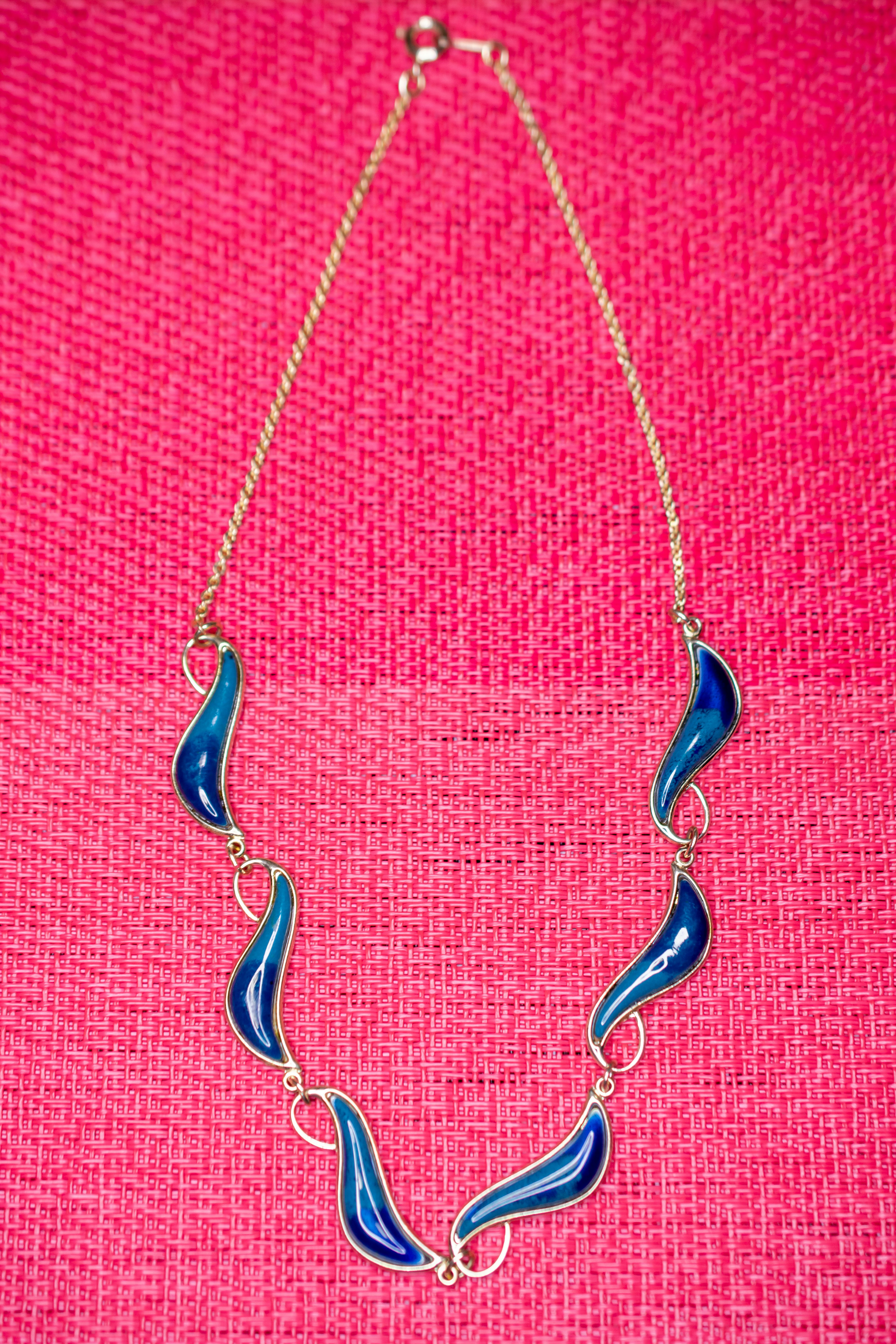 Blue wave-shaped pendant hanging from a gold chain