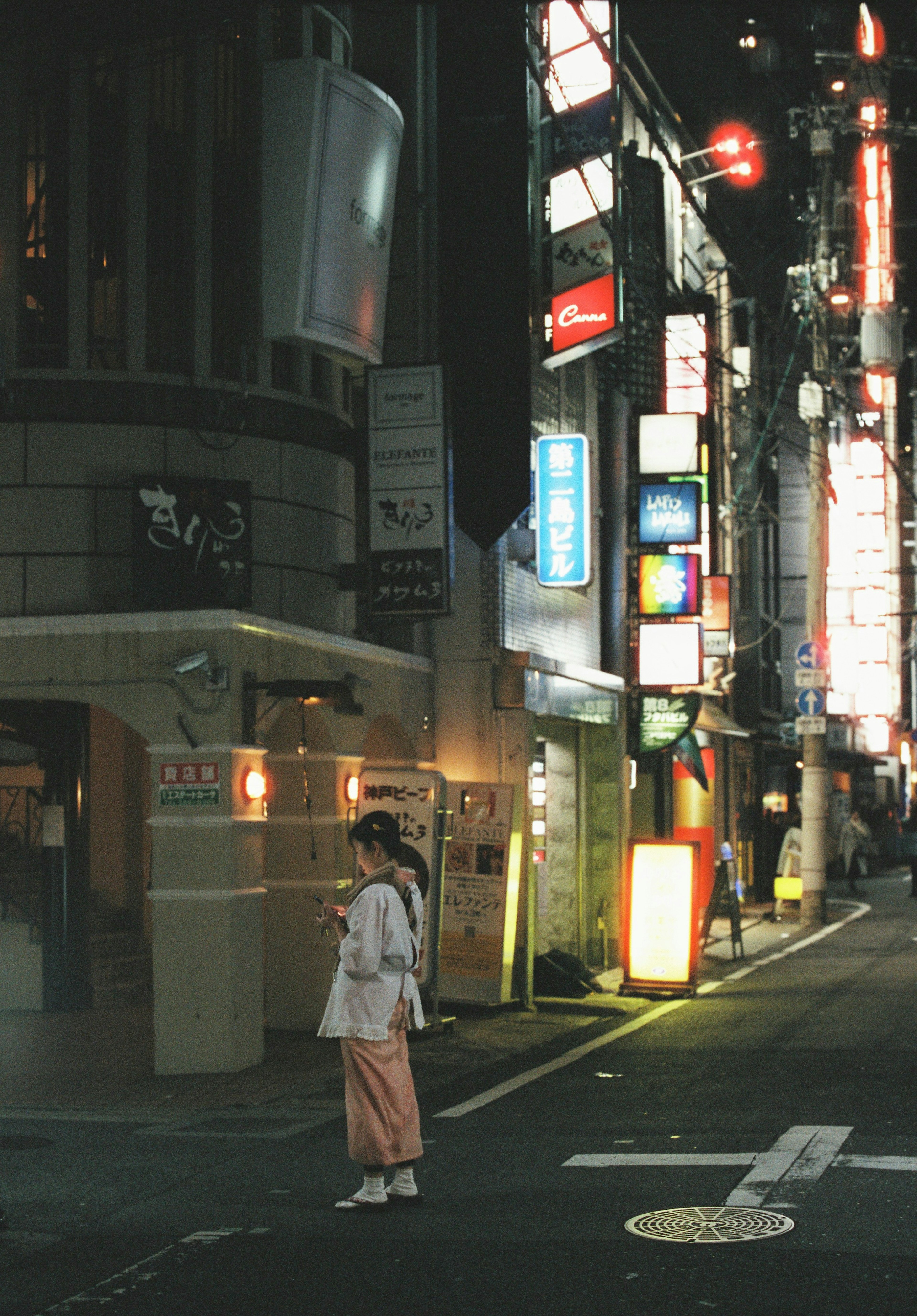 A woman standing at a street corner illuminated by neon signs at night