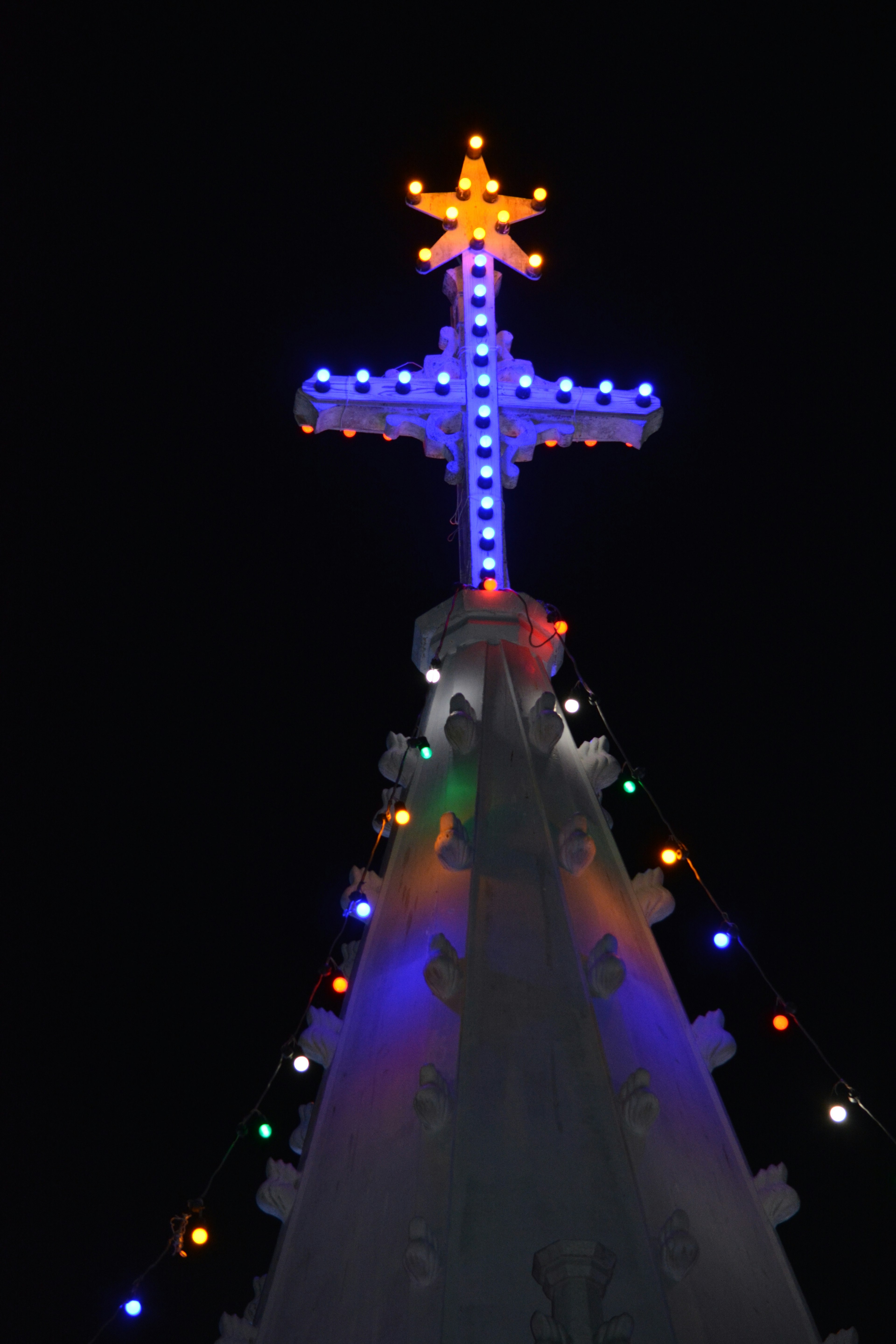 Bunte sternförmige Kreuzspitze auf einem Weihnachtsbaum, der im Nachthimmel leuchtet