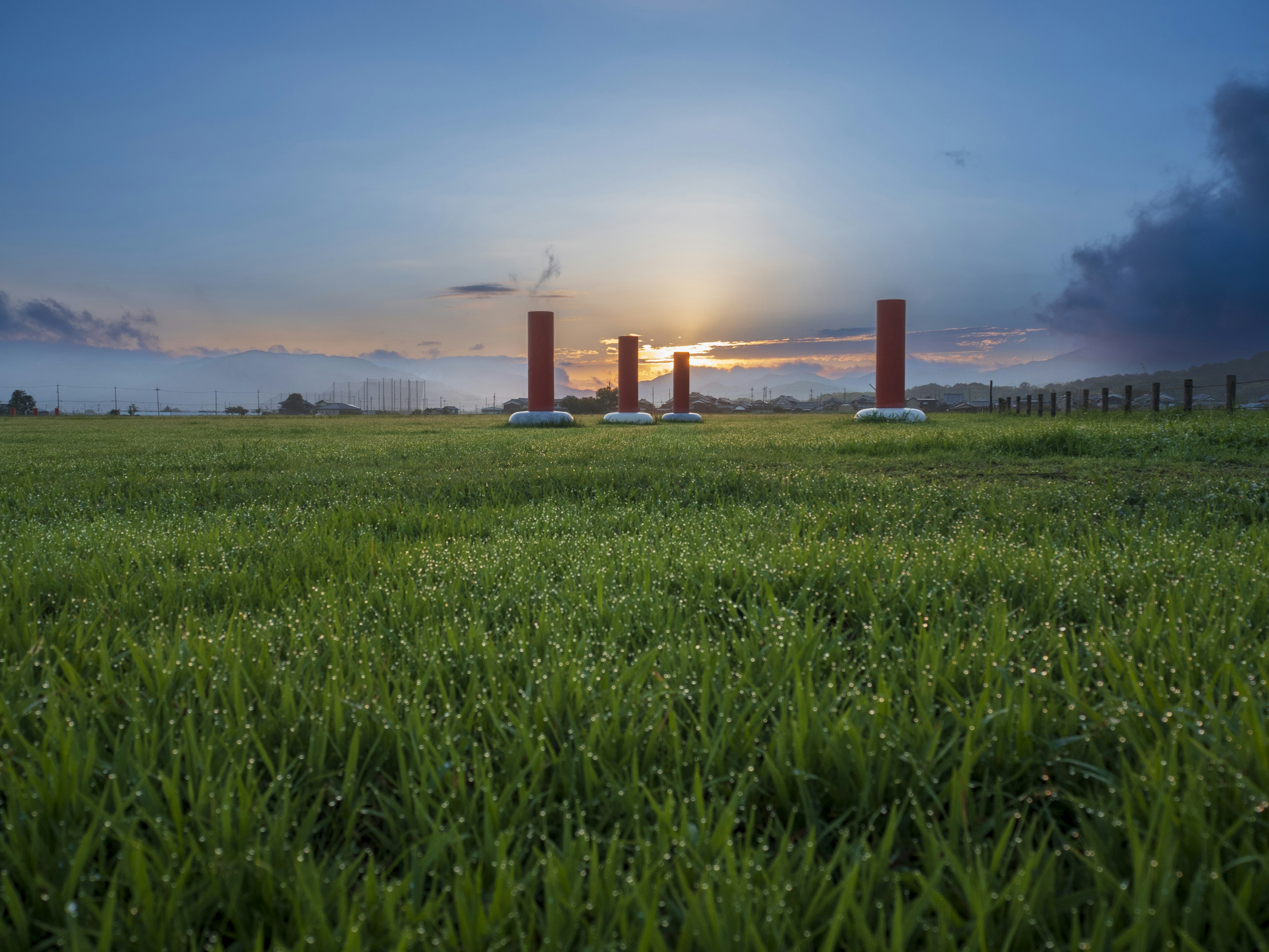 Green grass field with red pillars at sunset